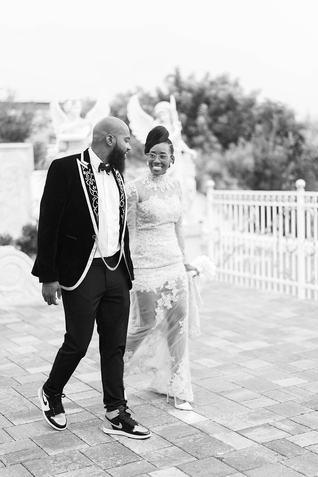 black and white image of bride and groom holding hands and walking through the outside of their wedding venue