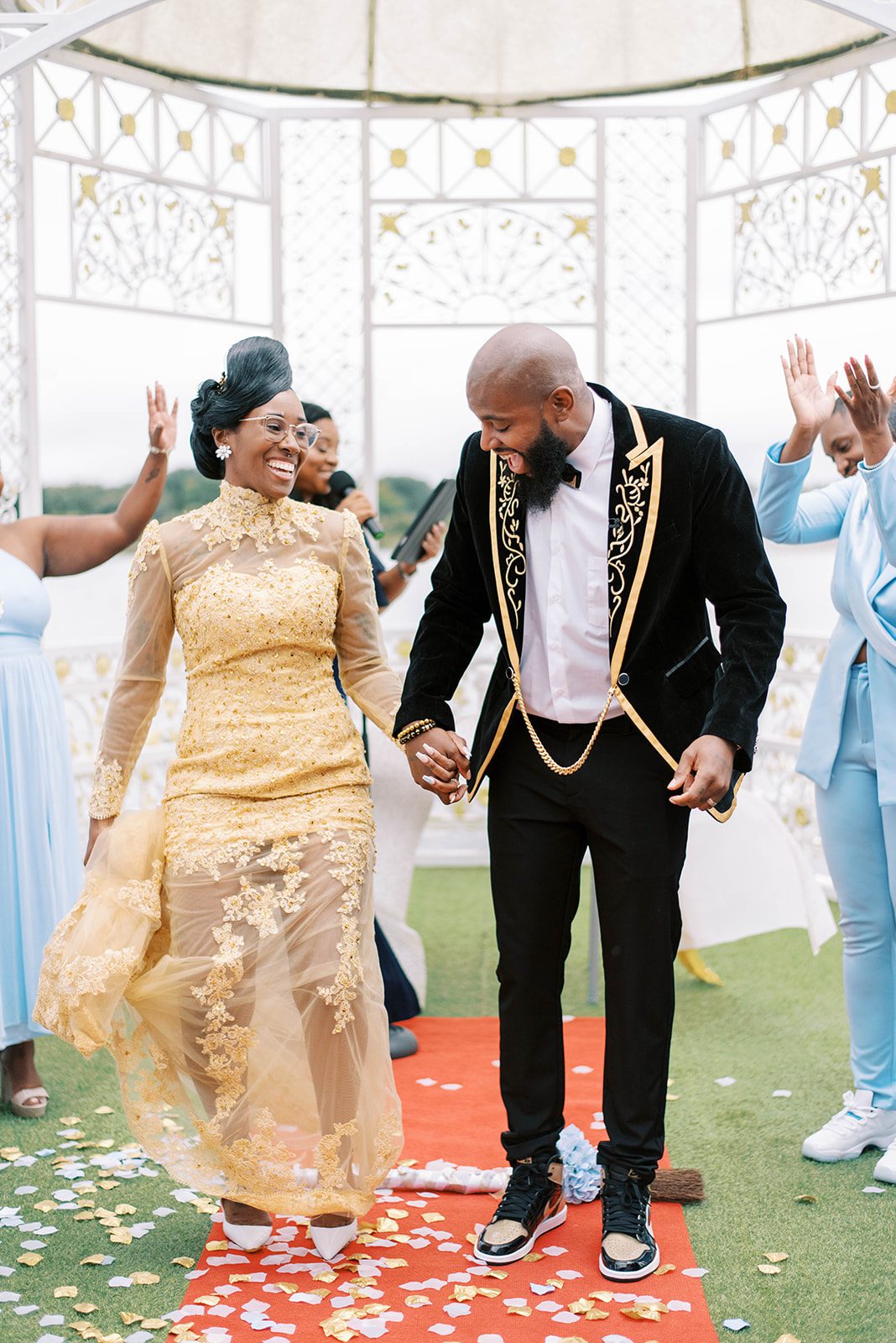 Chic Venue Tampa Wedding with bride and groom walking away from the ceremony as they hold hands and smile together in their gold wedding attire