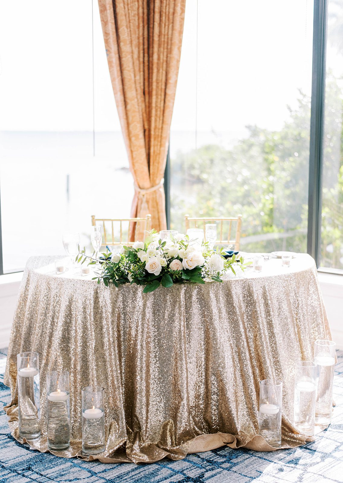 bride and grooms table with a gold sequence table cloth with white wedding flowers as decor at the Rusty Pelican