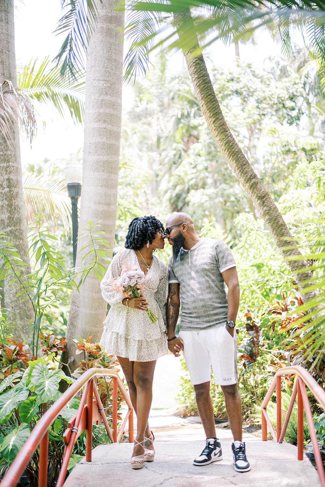 Tampa Florida engagement session with man and woman holding hands and walking over a bridge in a lush tropical garden