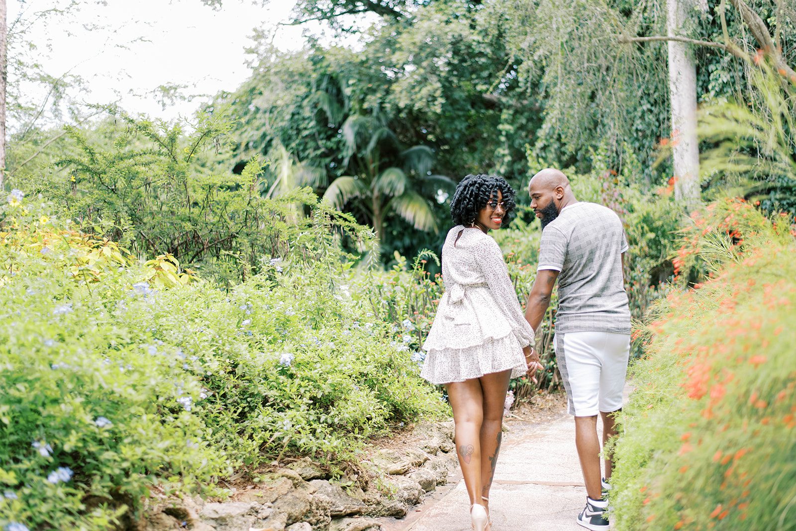 engagement photo with man and woman holding hands and walking away from the camera as they look back over their shoulders, captured by Tampa Bay wedding photographer
