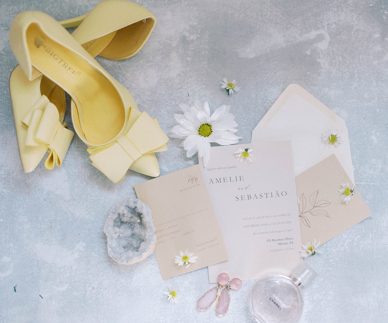wedding flatlay with soft yellow pointed heels and daisies surrounding a pretty pink wedding invitation
