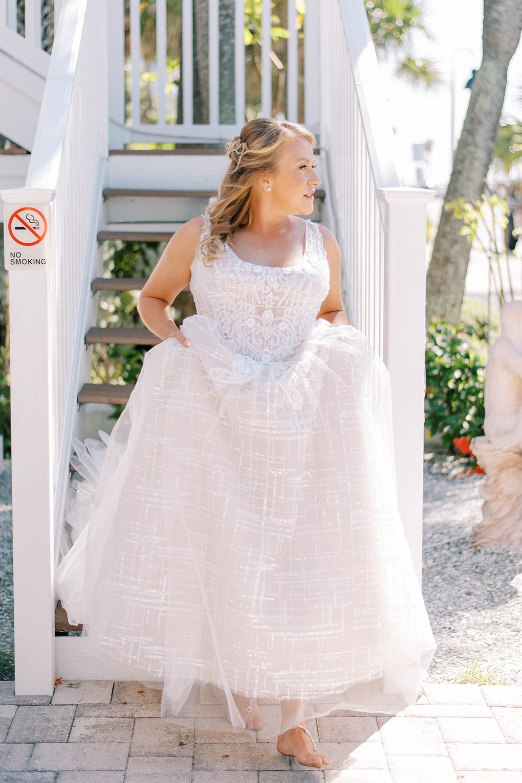 bride walking down the stairs of a beach house in her wedding dress as she goes to have her first look with her groom on her Florida beach wedding day