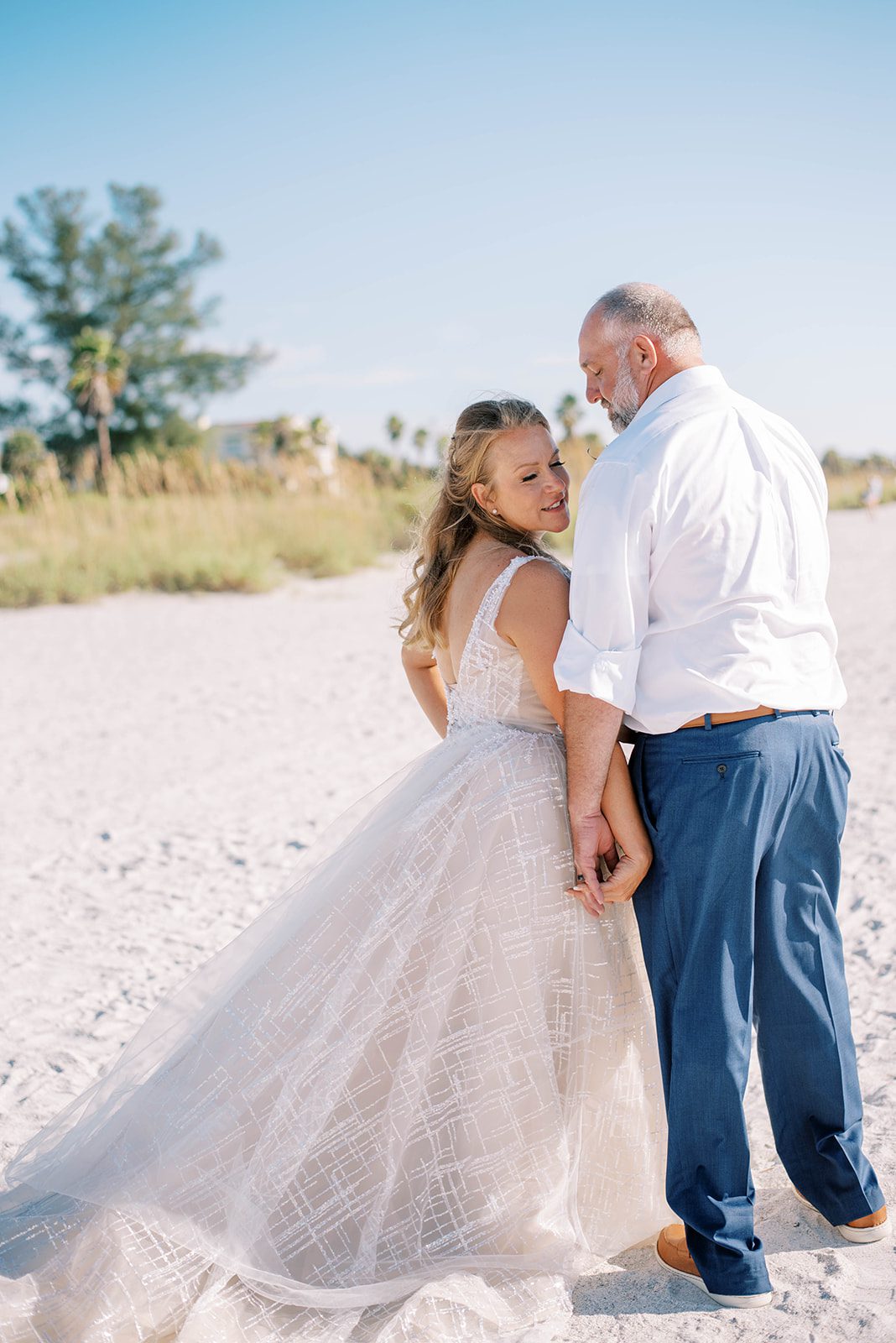 bride holding hands with her groom on a beach in Florida as the couple faces away from the camera and the bride looks over her shoulder