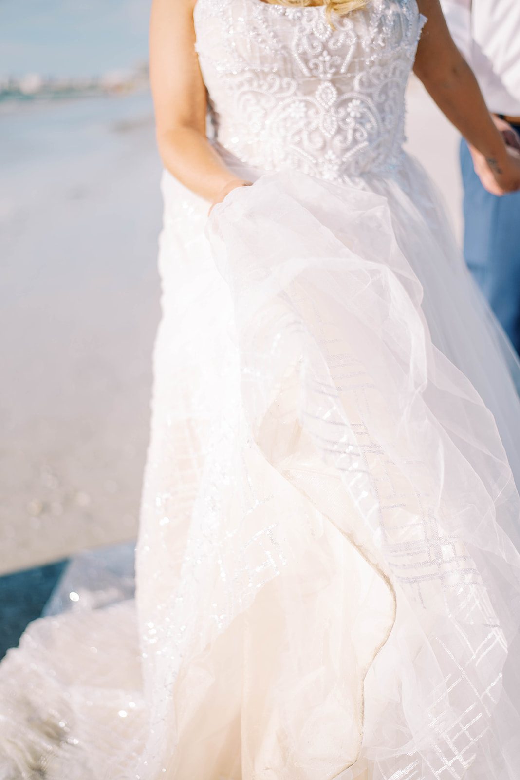 bride walking on the beach while holding her ruffled wedding dress as the sunsets