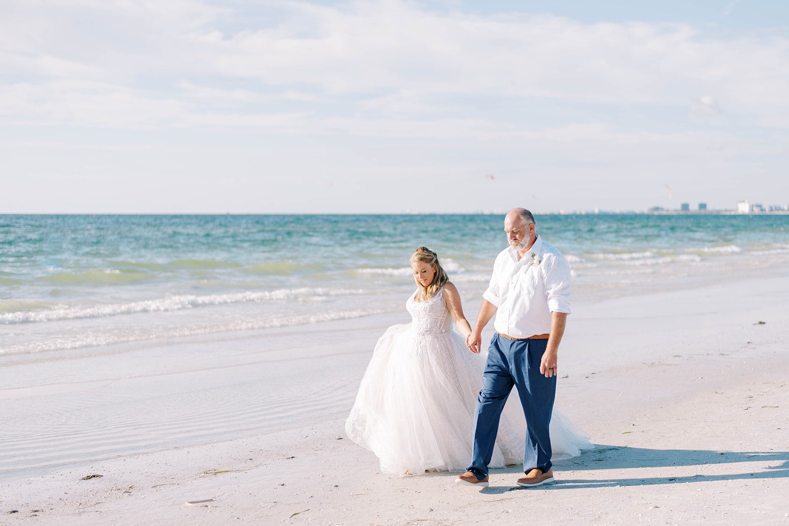 bride and groom at St. Petersburg beach holding hands while they walk together on their wedding day