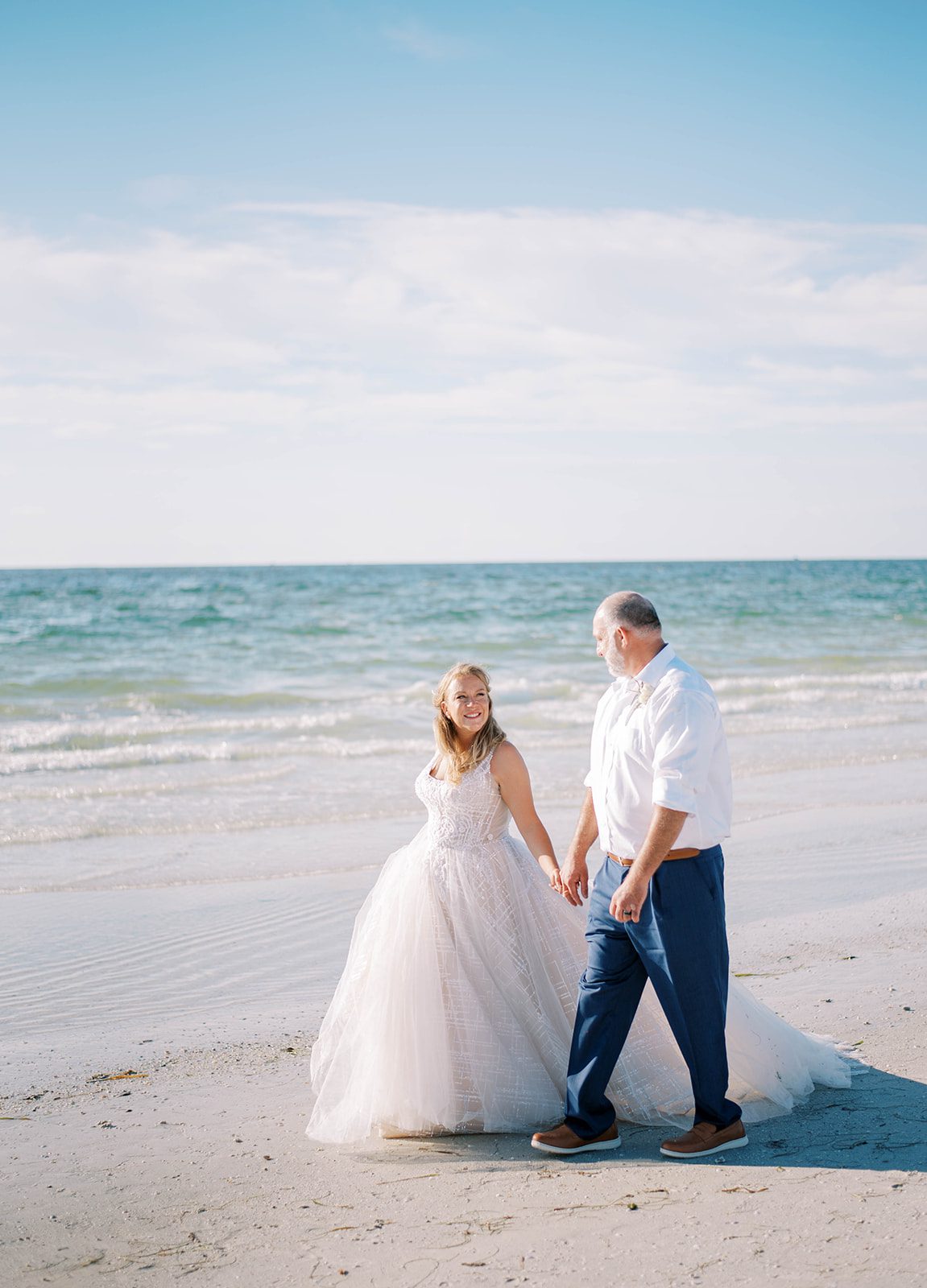 luxury destination beach wedding in Florida with bride and groom walking on the beach while holding hands on a beautiful clear day