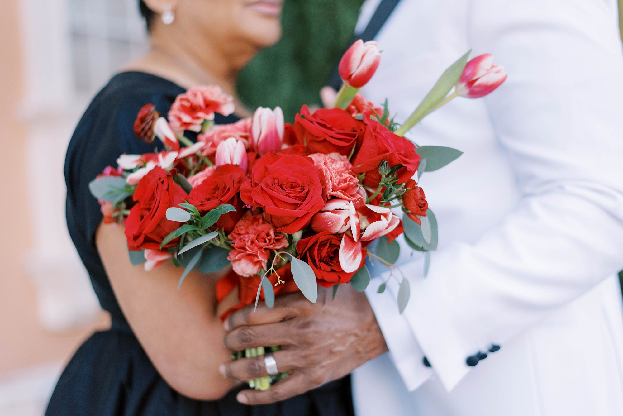 bride and groom hold bouquet of red roses, carnations and tulips