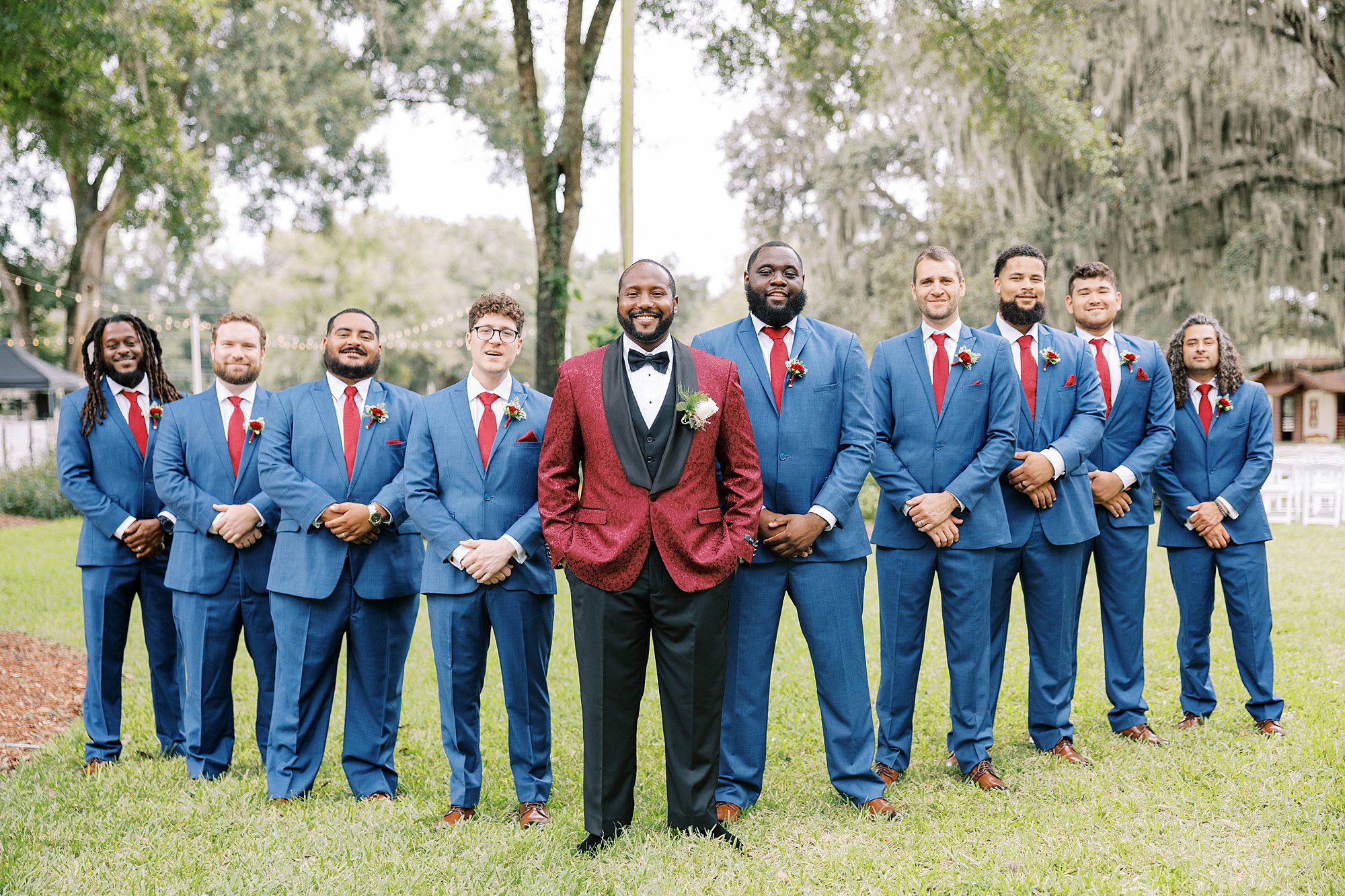 groom in red suit jacket poses with groomsmen in navy suits