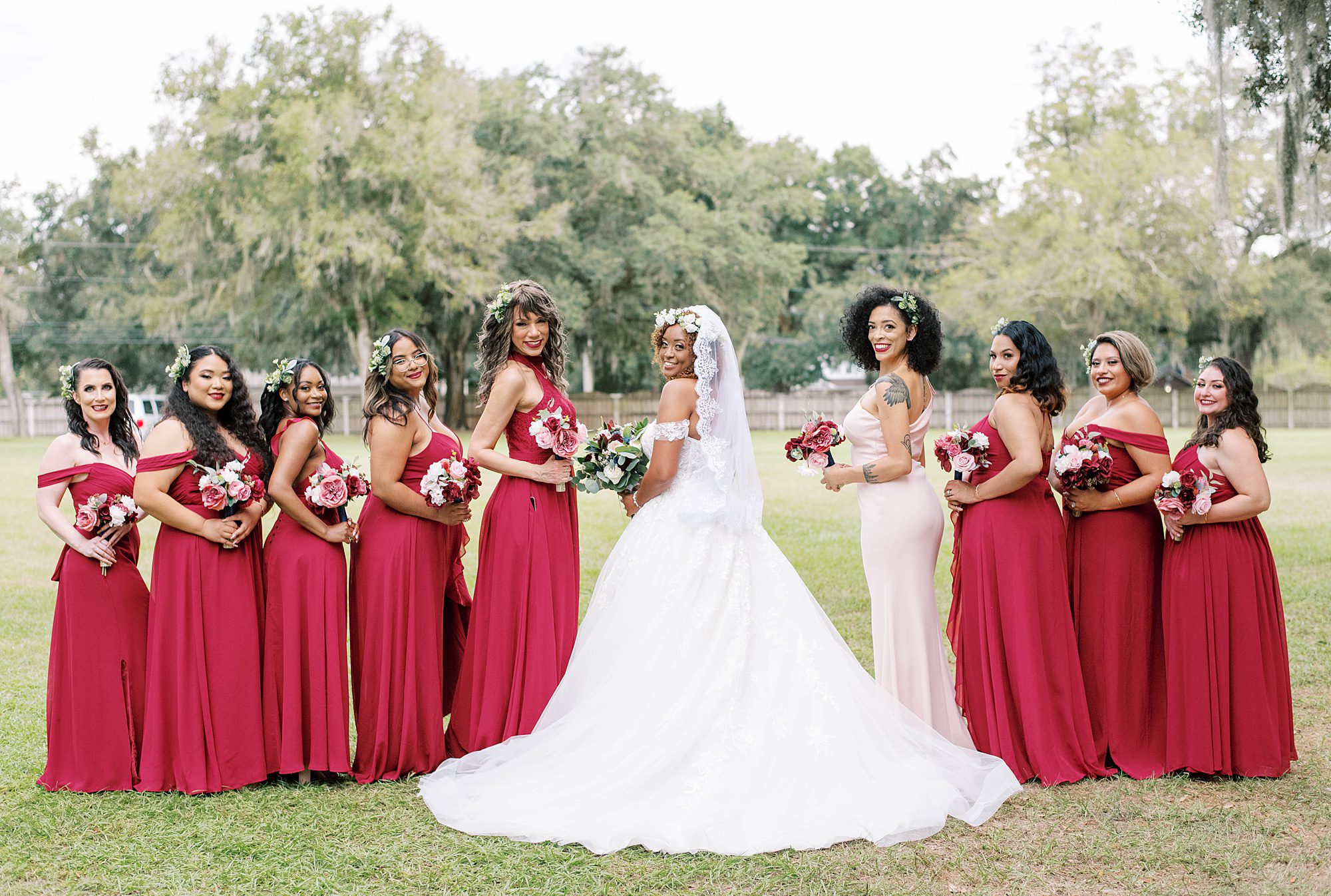bride looks over shoulder while standing with bridesmaids in red gowns
