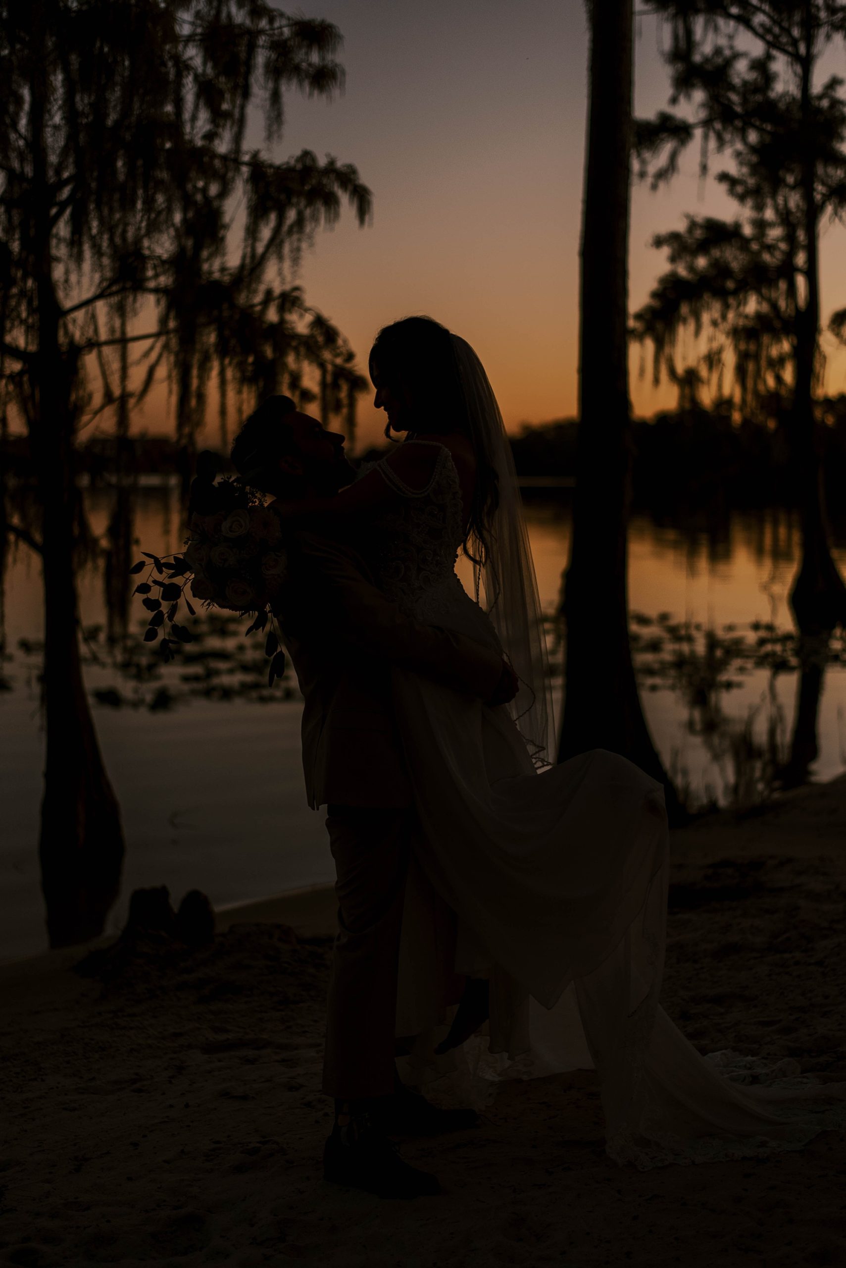 groom lifts bride up at sunset silhouette photo