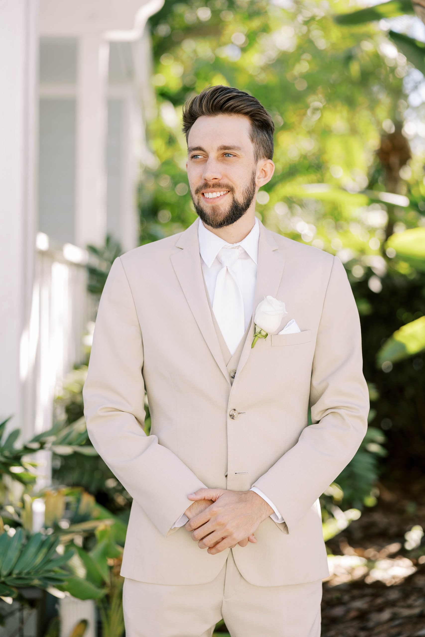groom stands with hands crossed in tan suit