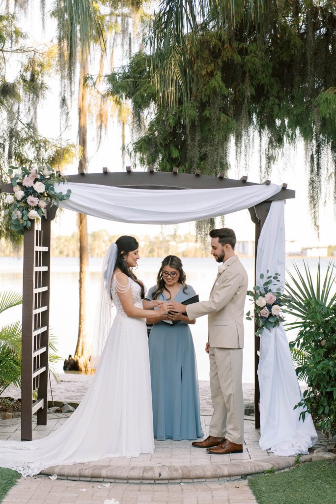 bride and groom exchange vows under wooden arbor with white drape