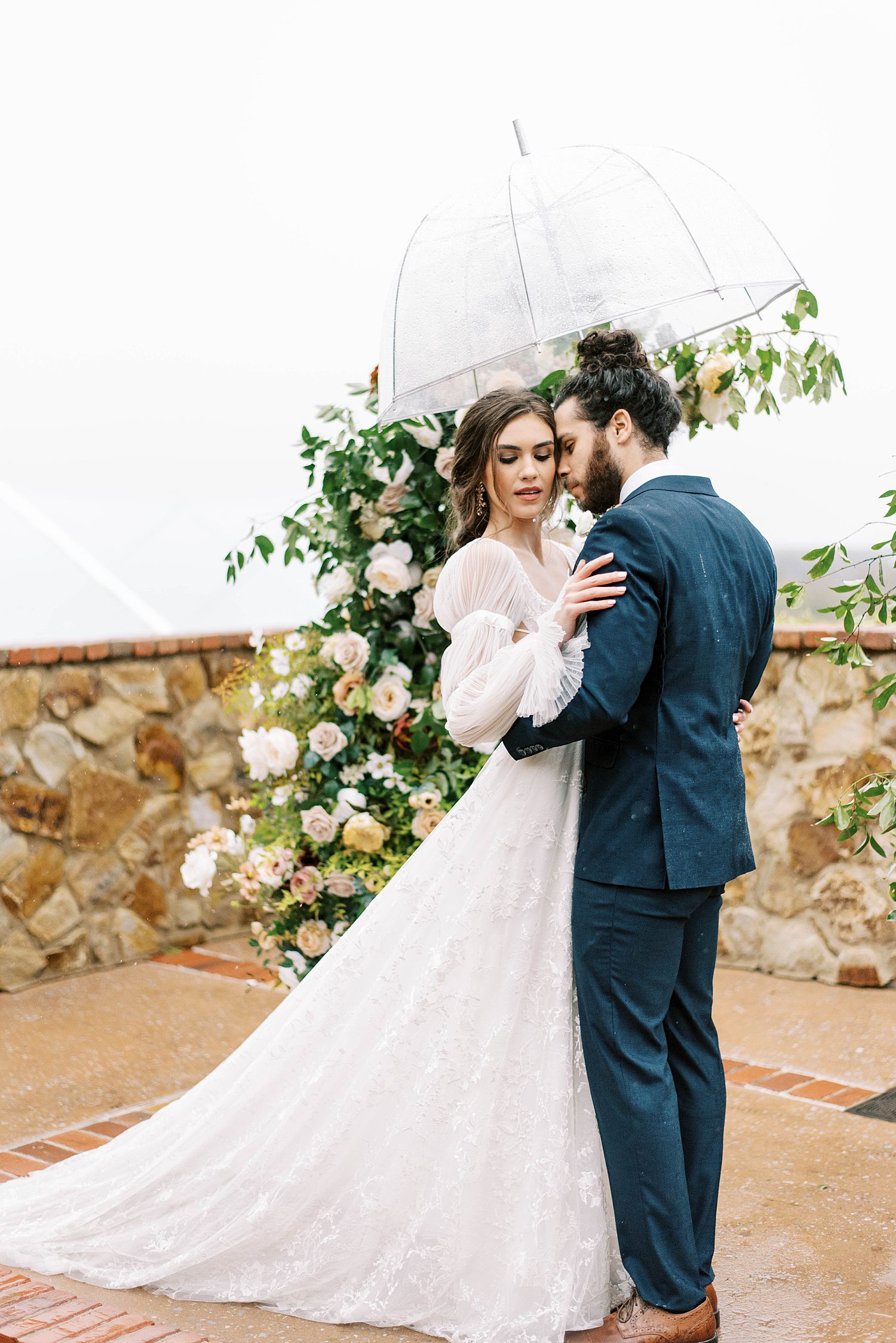 couple hugs under umbrella during rainy wedding day