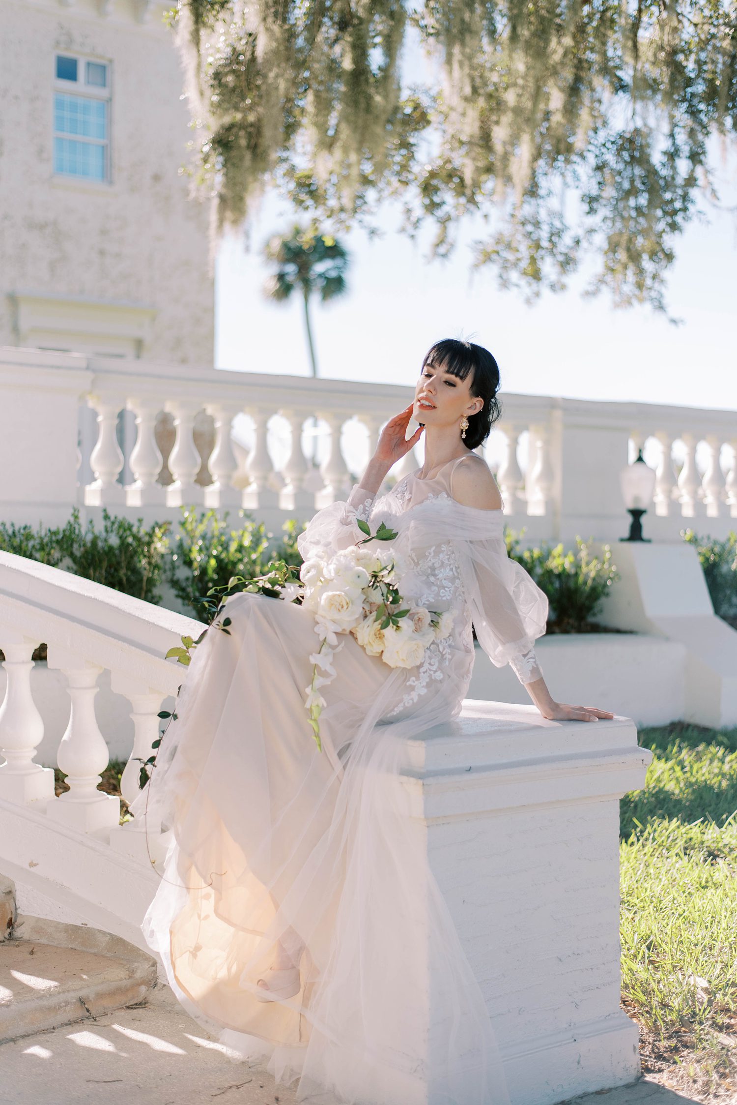 bride in off-the-shoulder gown sits on end of staircase