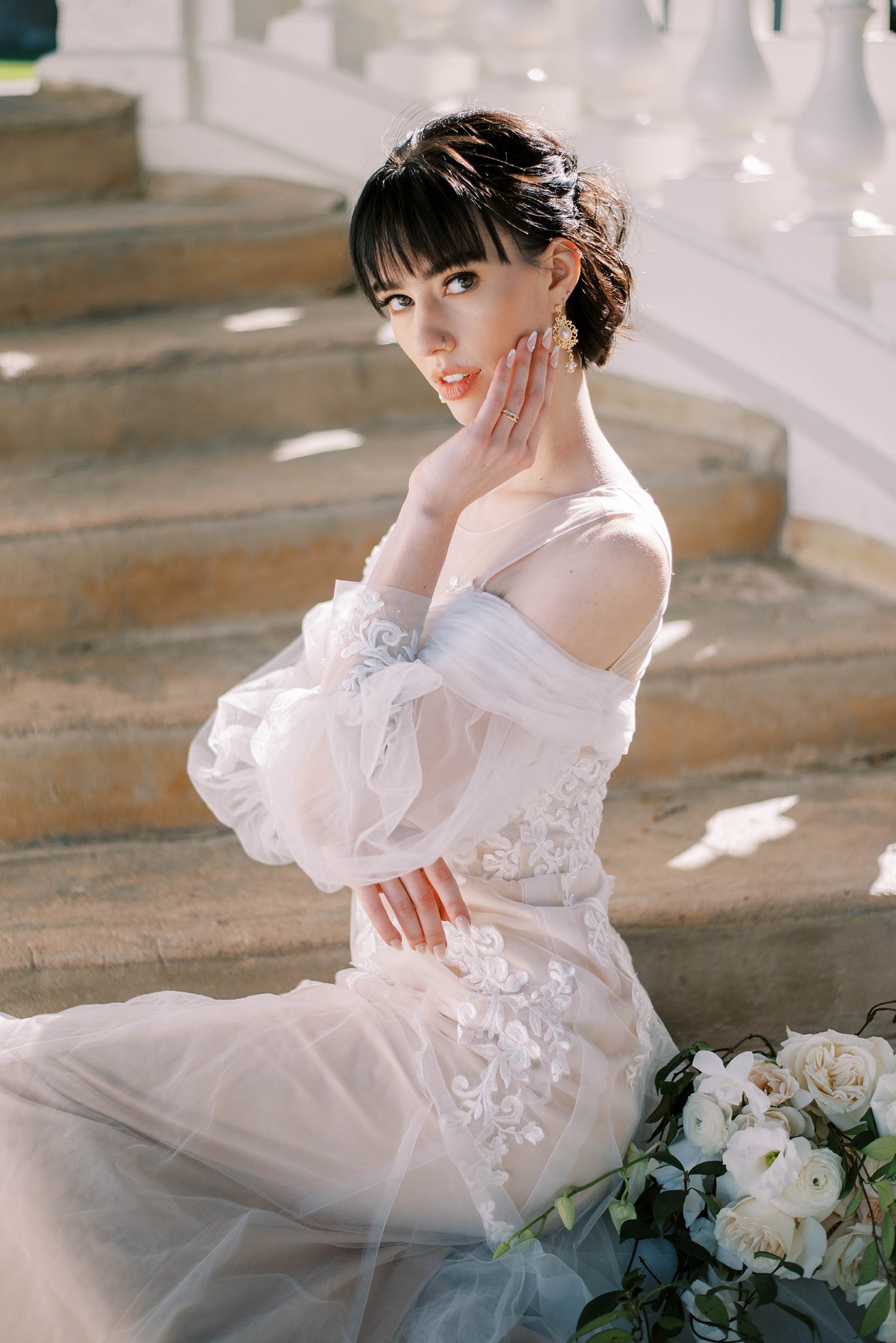 bride sits on steps in off-the-shoulder gown