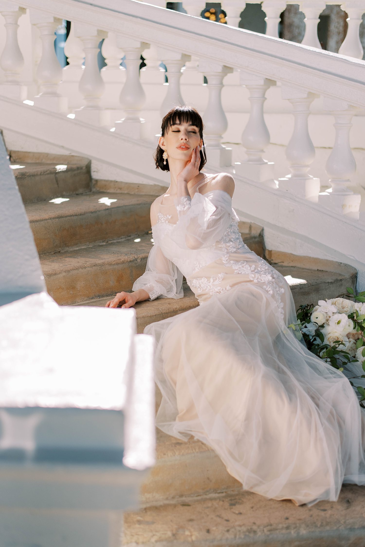 bride sits on steps in off-the-shoulder wedding gown