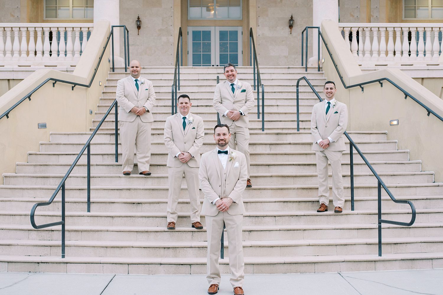 groom stands on steps at The Regent with groomsmen in tan suits