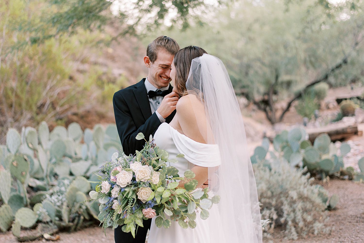 bride and groom stand by group of cacti in desert