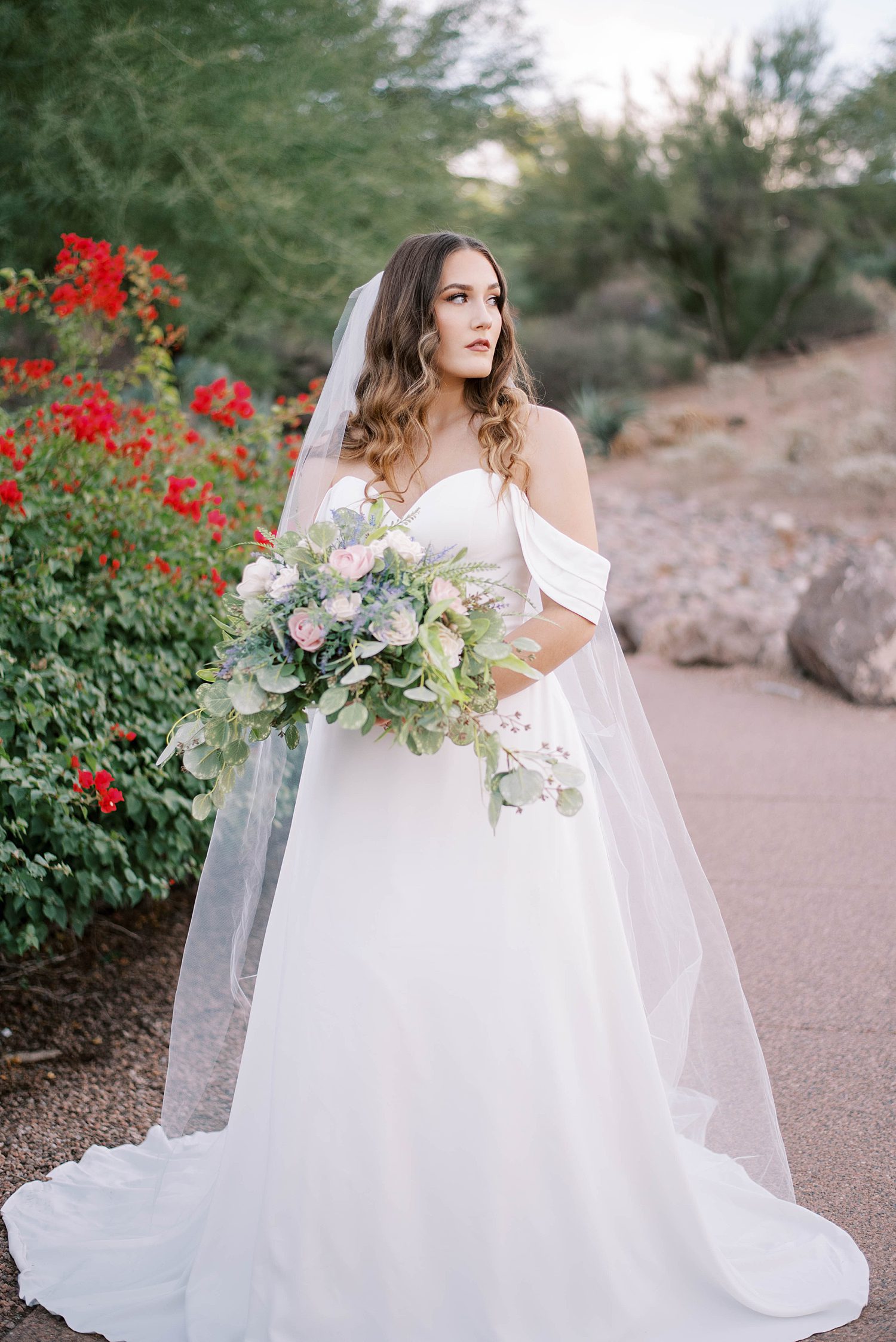 bride stands in desert holding bouquet with veil draped around shoulders