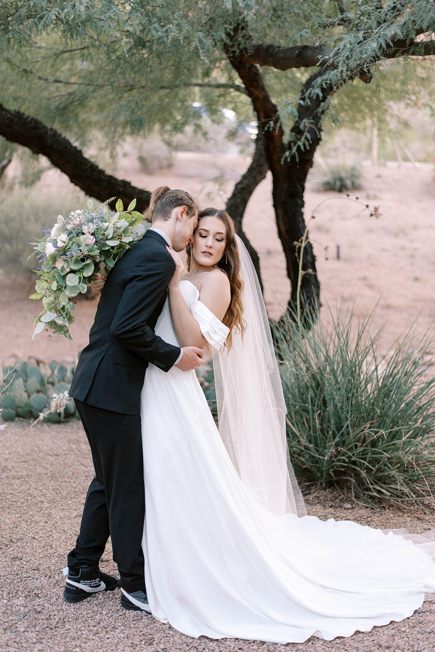 groom kisses bride's neck standing by tree at Buttes Marriott Hotel