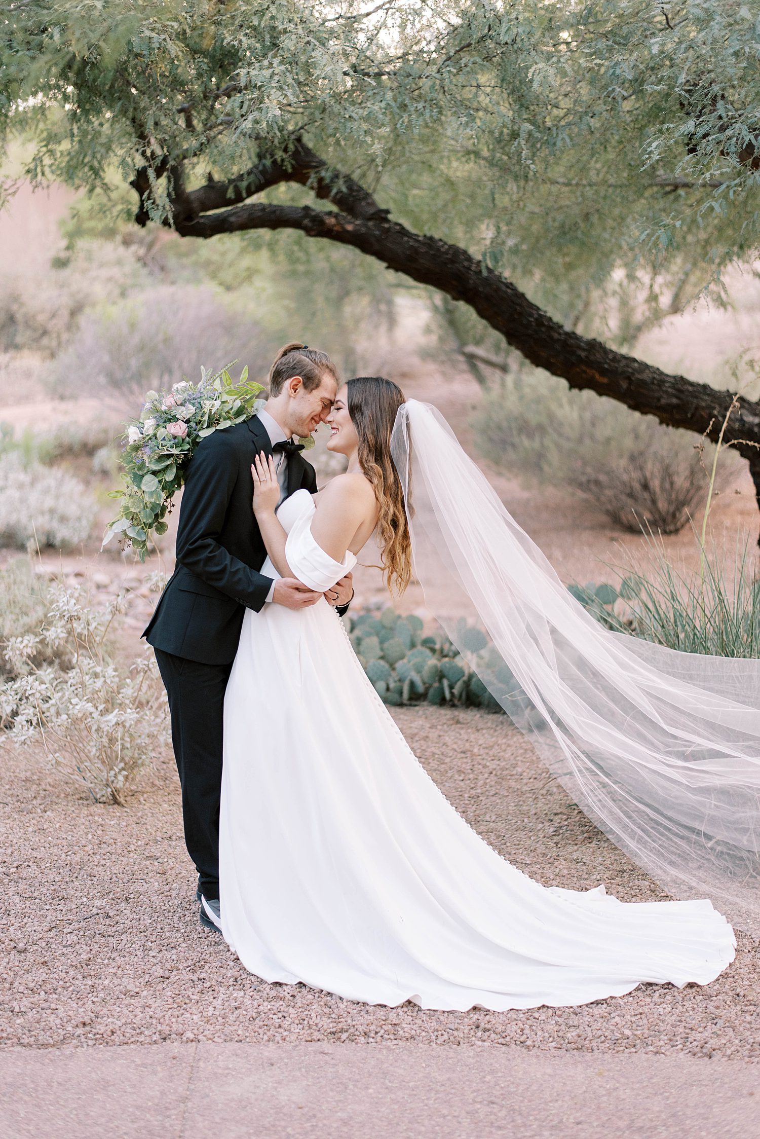 newlyweds kiss by tree in desert during destination wedding day