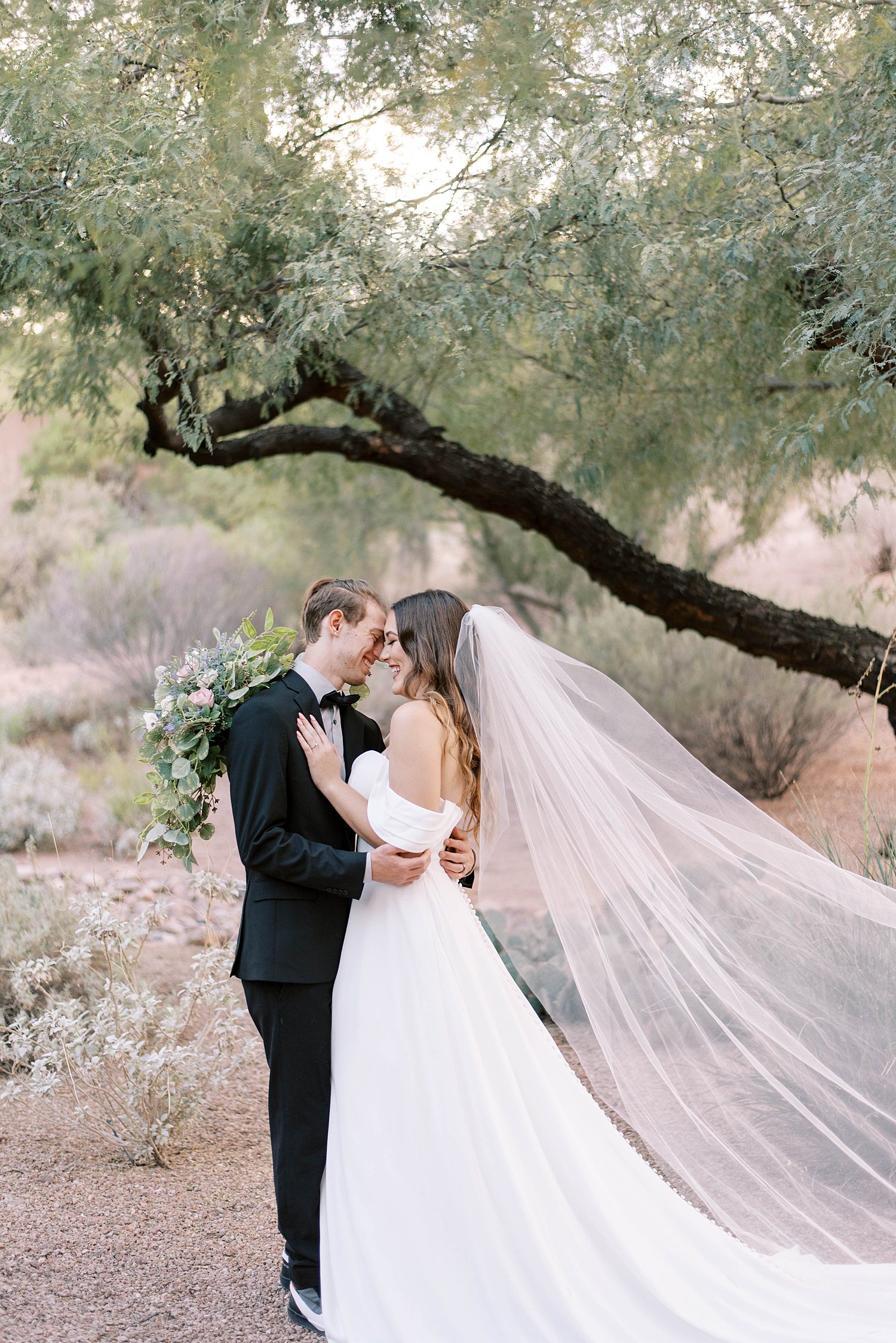 bride and groom stand together under tree at Buttes Marriott Hotel