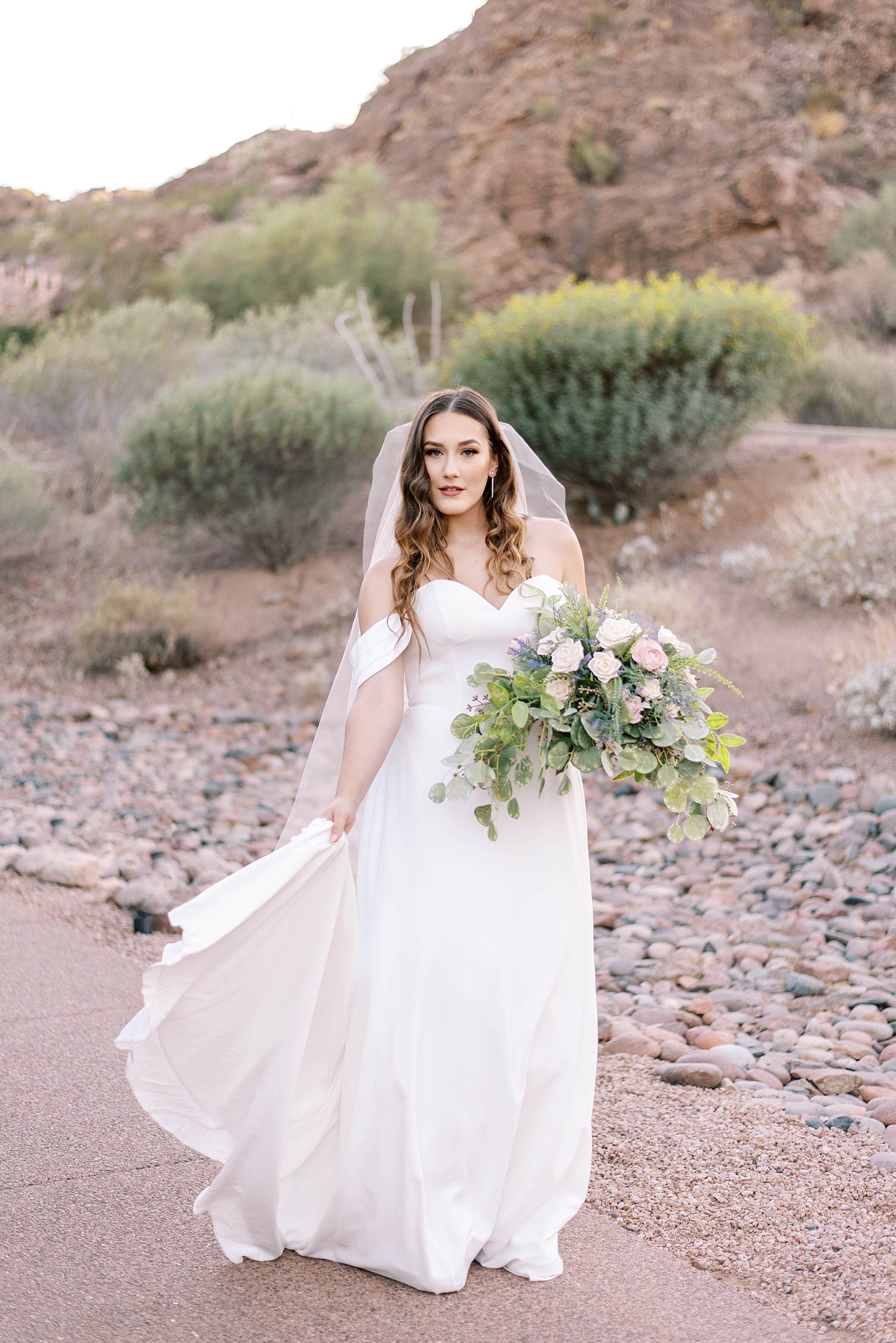 bride walks holding skirt through desert in Arizona