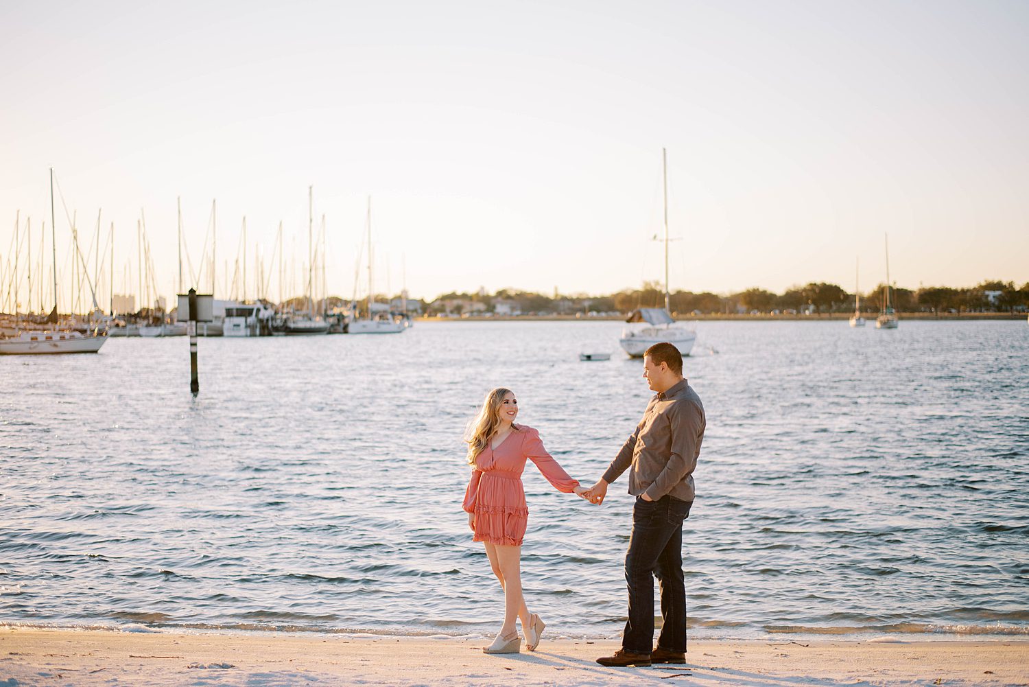 couple holds hands walking along beach at Davis Island