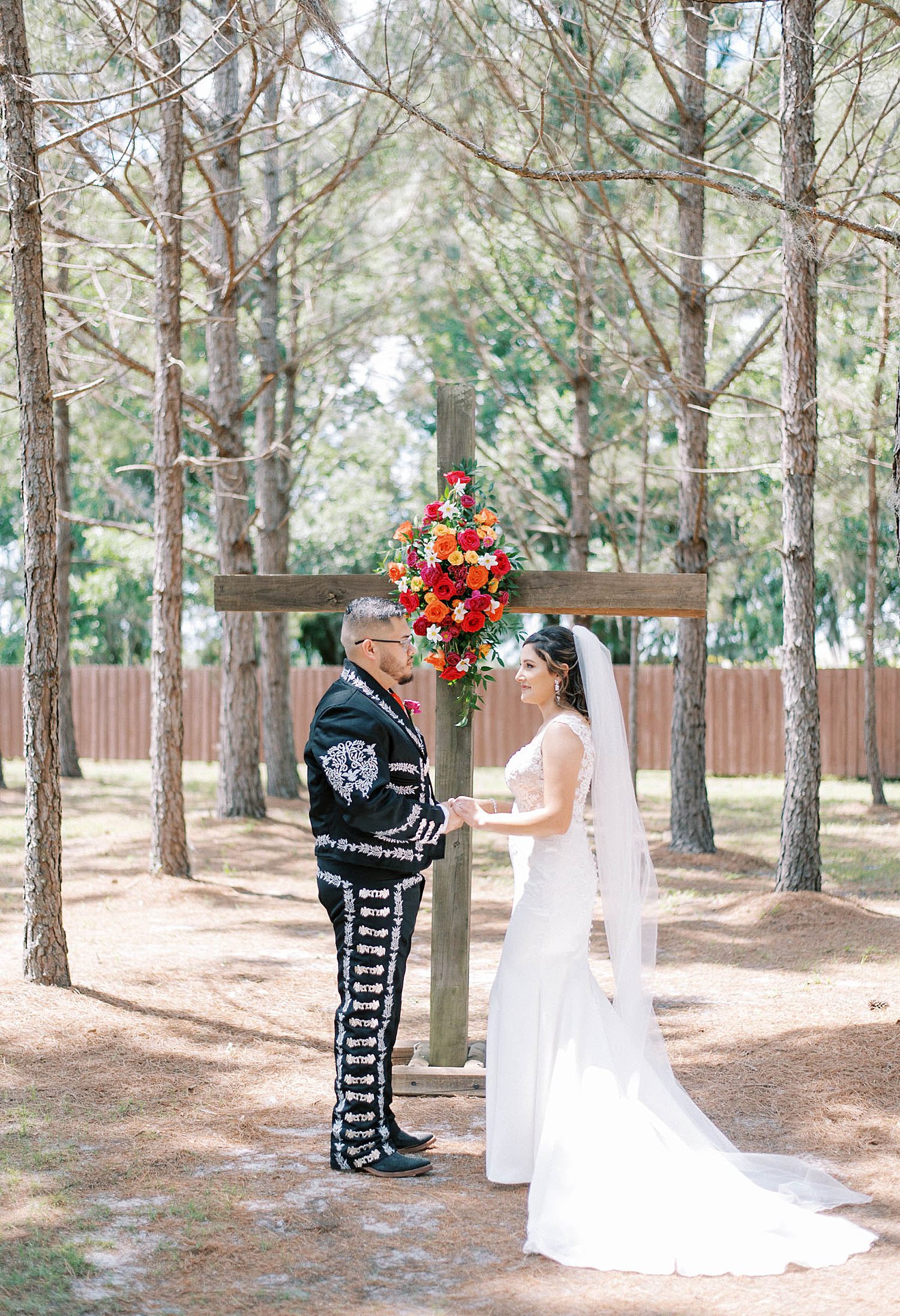 bride and groom hold hands by wooden cross at The Barn at Lone Oak Acres