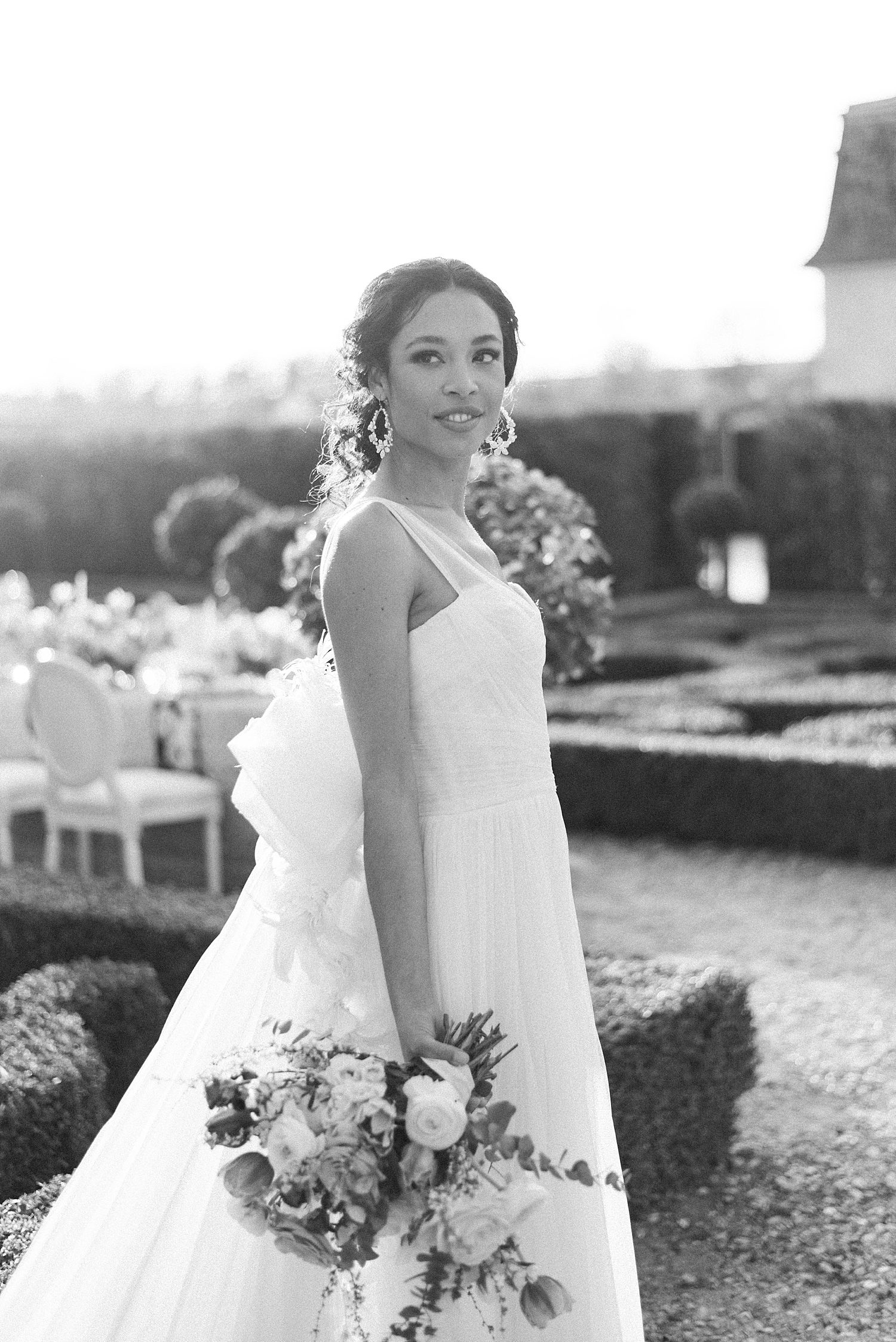 bride stands showing off Marchesa bridal gown in gardens of Chateau de Villette