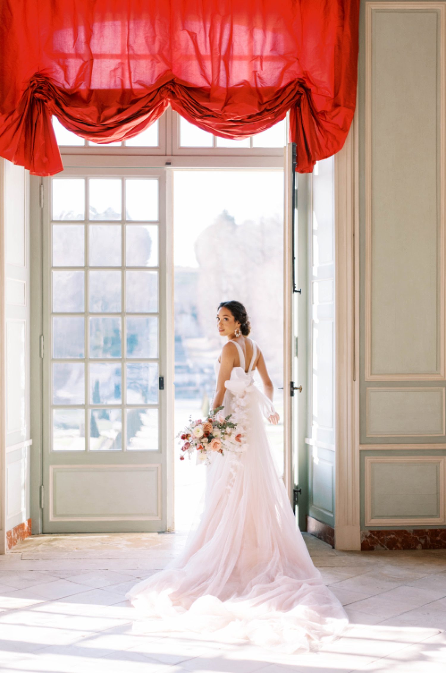 bride stands in window of Chateau de Villette looking over shoulder in blush gown 