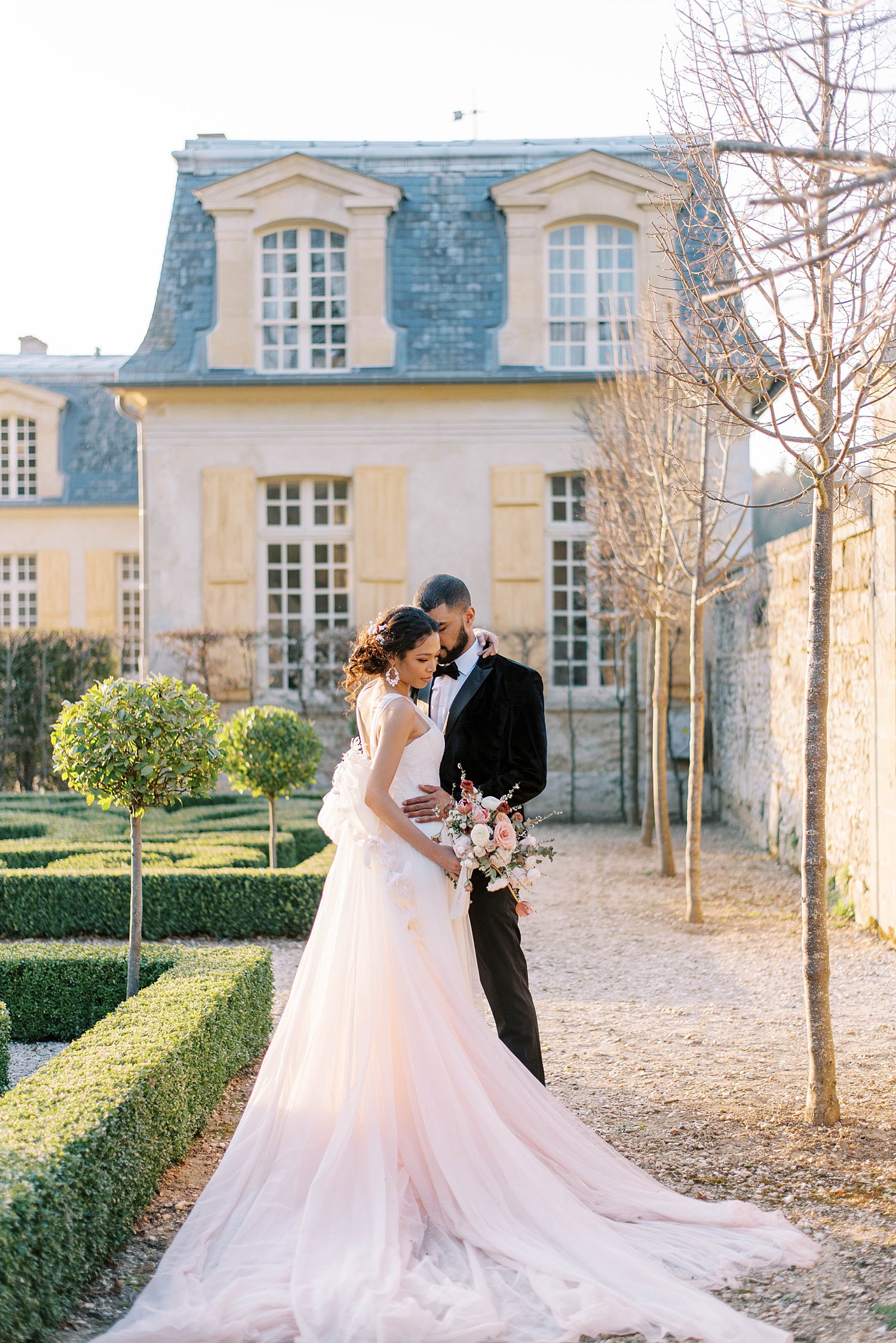 bride and groom hug with bride's blush train around them on path outside Chateau de Villette