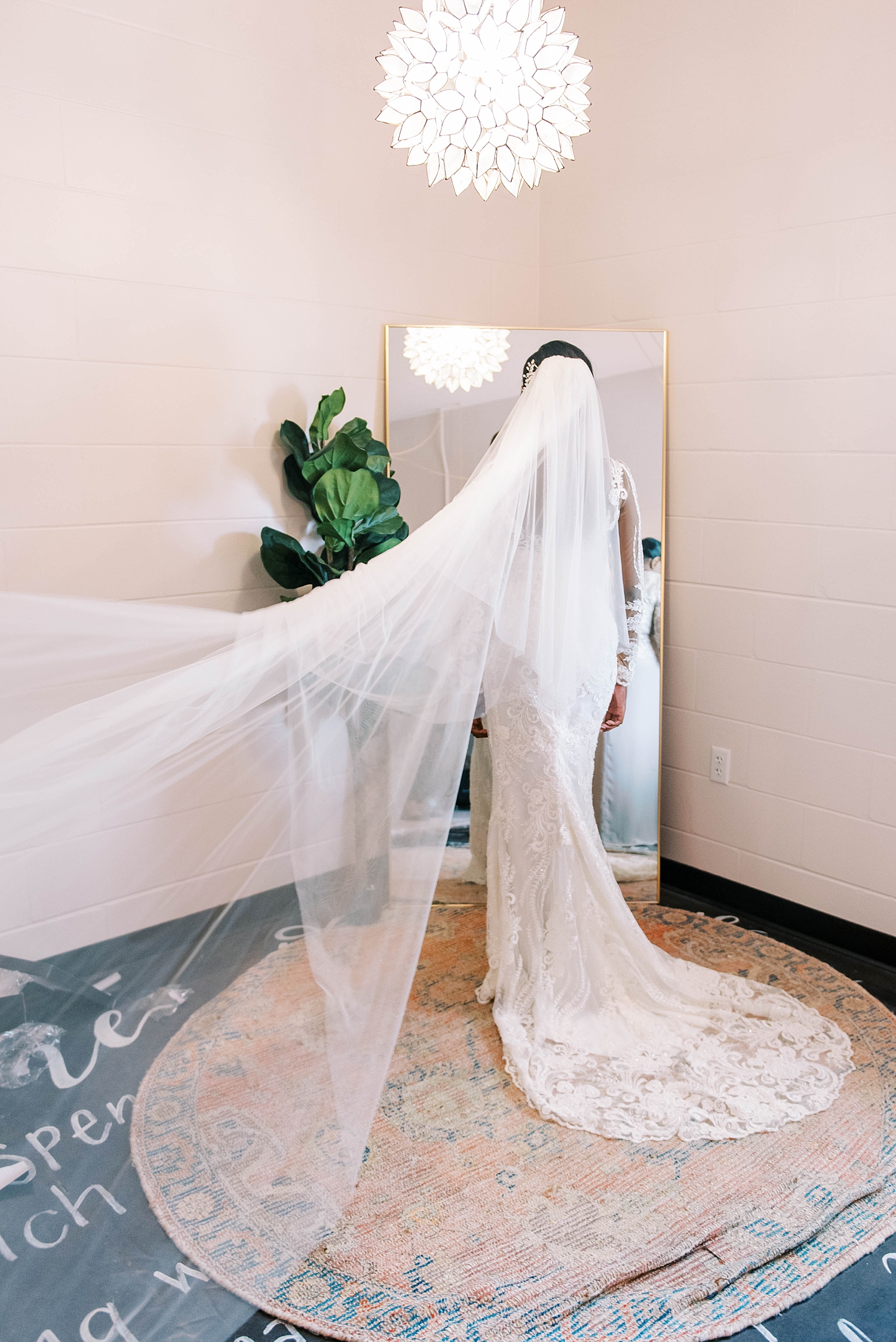 bride poses in mirror with veil pulled behind her