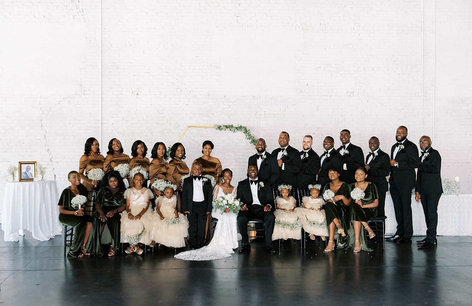 bride and groom pose with wedding party in green and gold gowns, classic black tuxes, and white florals at Haus 820