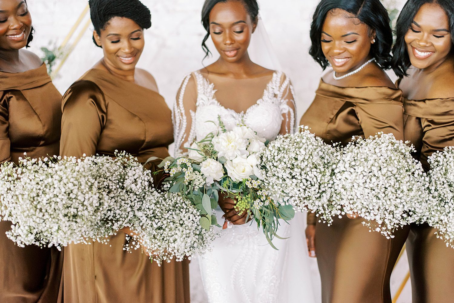 bride holds bouquet of white flowers with bridesmaids holding baby's breath