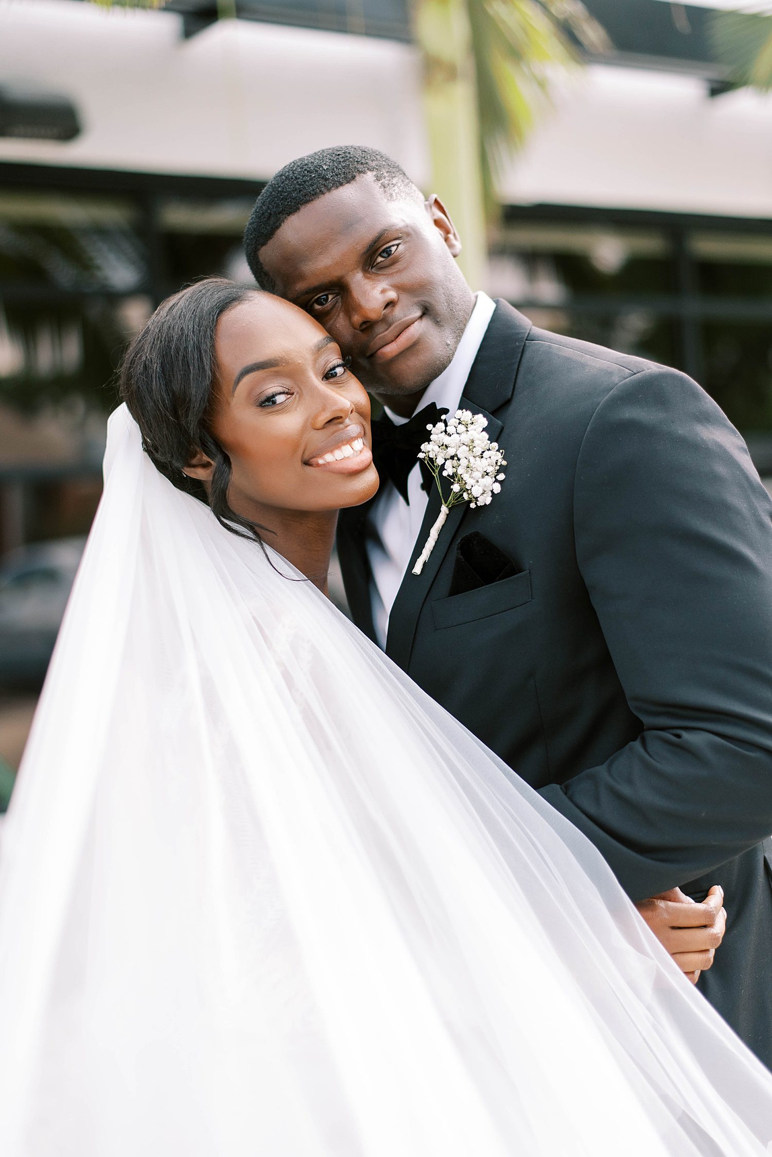 couple leans heads together smiling during wedding portraits outside Haus 820