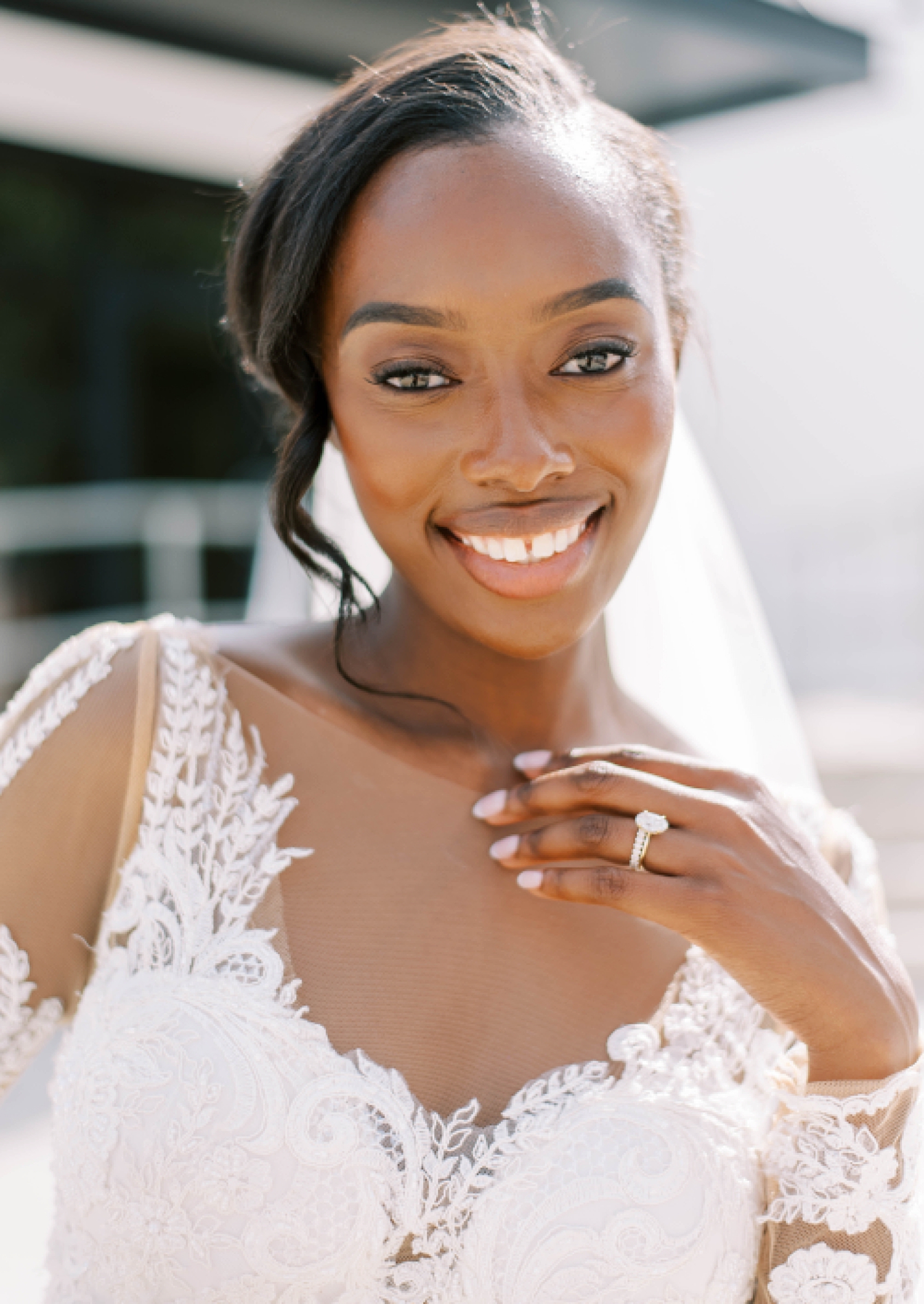 bride smiles showing off diamond ring with lace detail of wedding gown