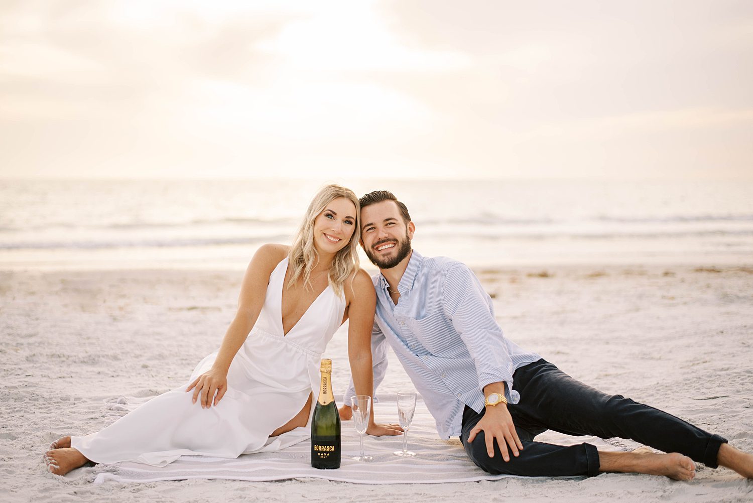 couple sits together on blanket during engagement photos on the beach at sunset in Florida 