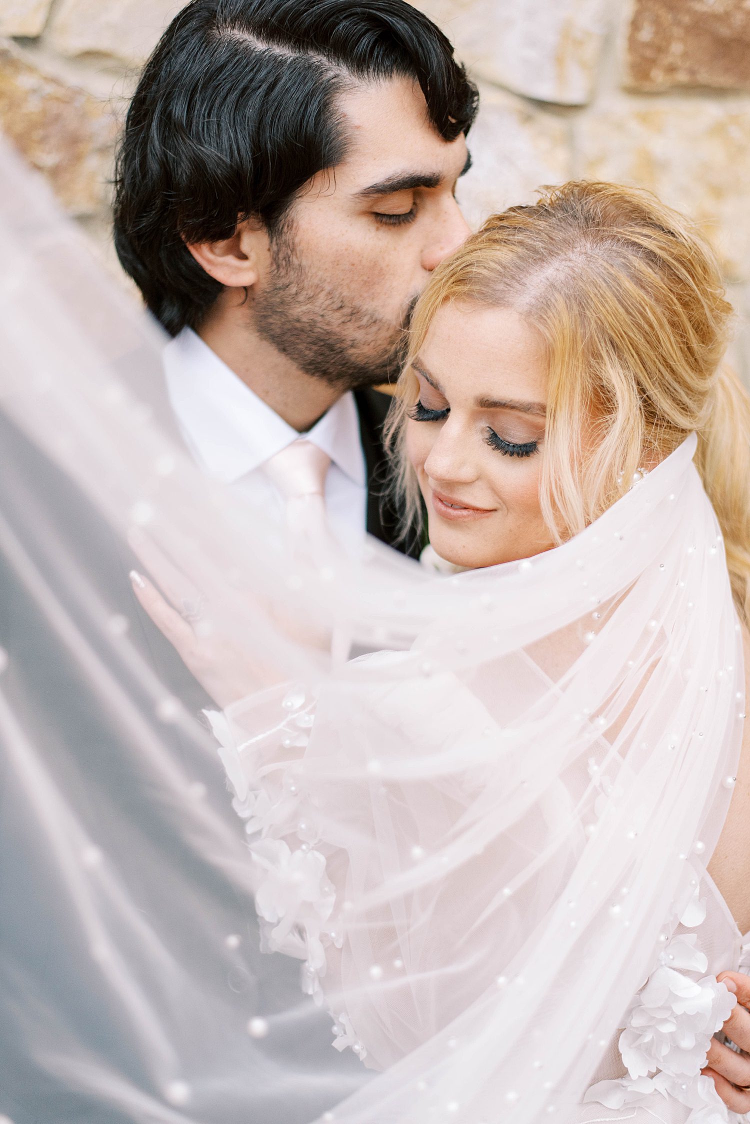 newlyweds hug with bride's veil draped around them