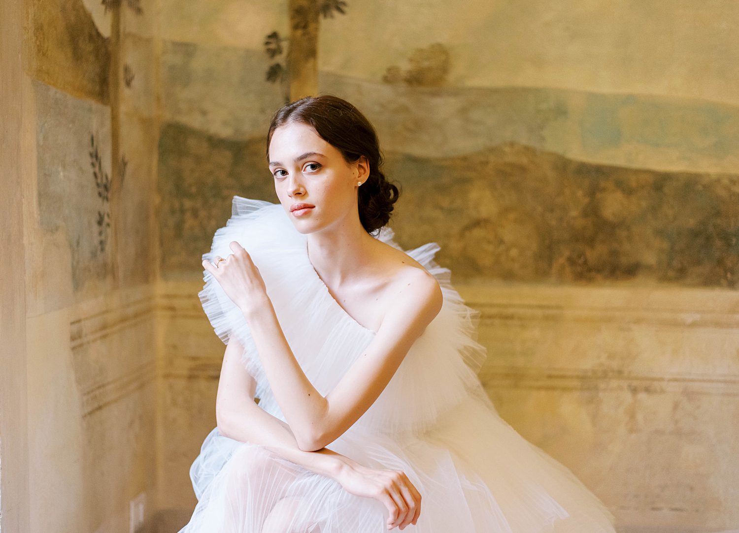 Italian bride sits in front of old frescos in hotel