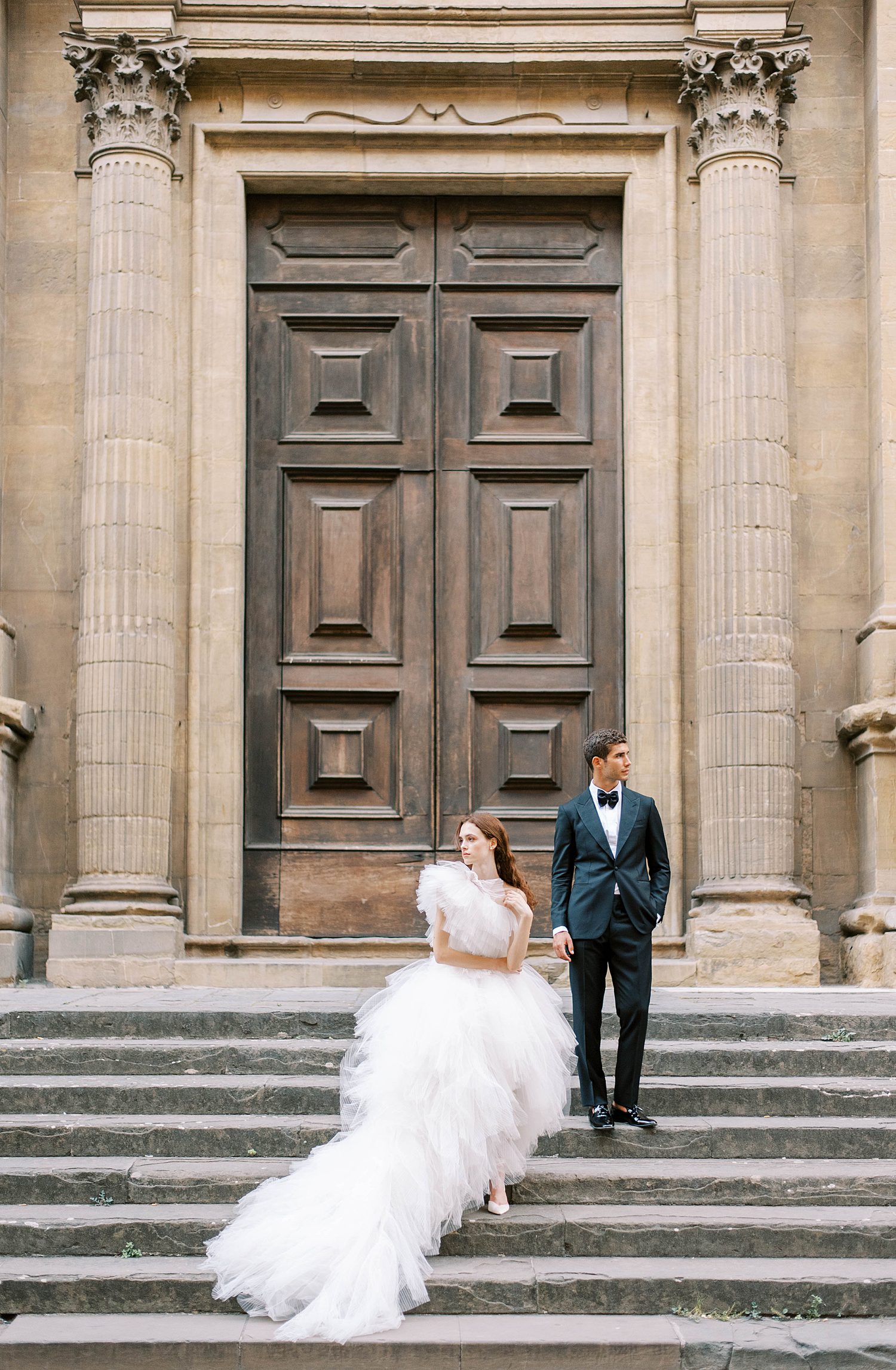 bride and groom stand on steps by wooden doors in Florence Italy 