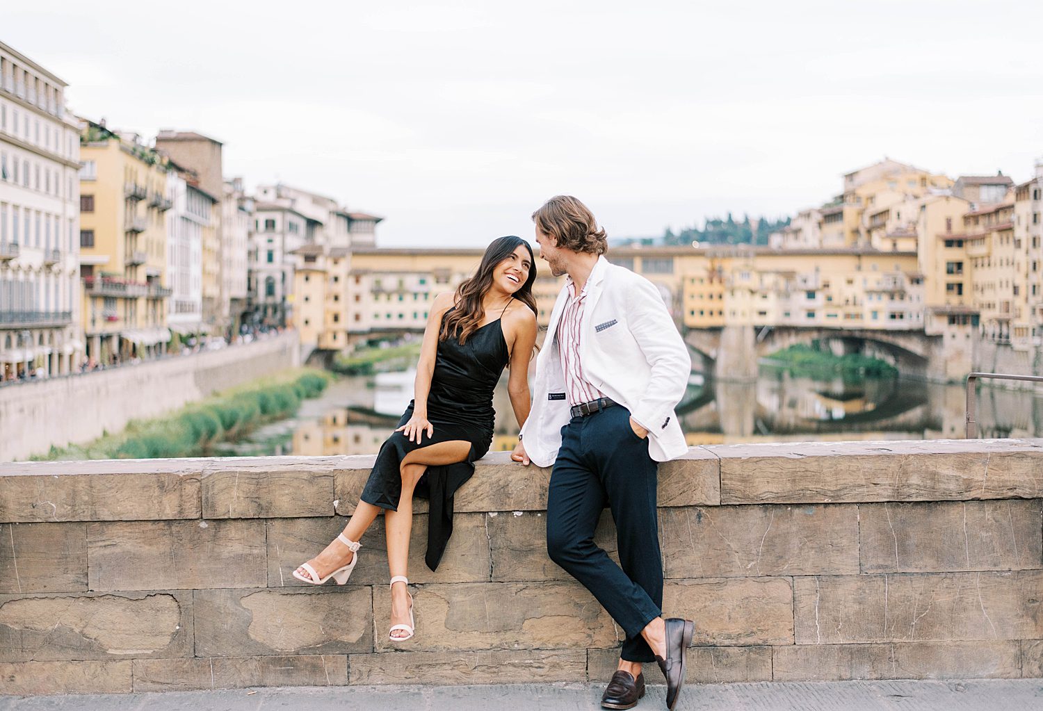 married couple laughs together sitting on stone bridge in Ponte Vecchio