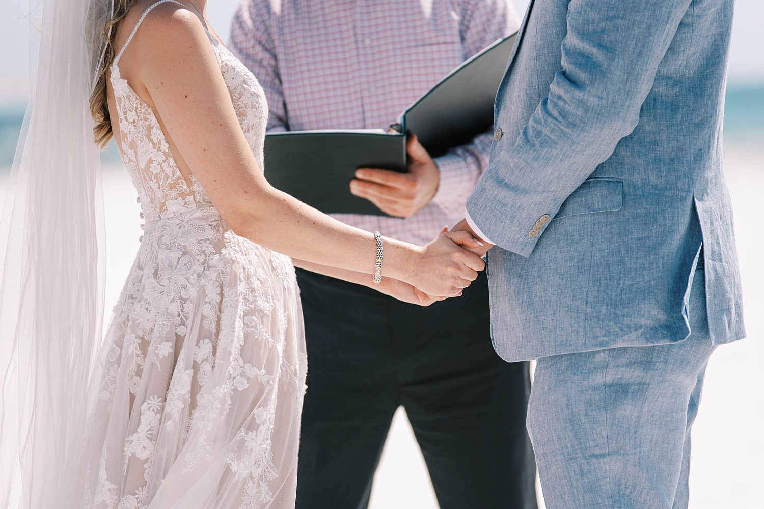 bride and groom hold hands during wedding ceremony on the beach