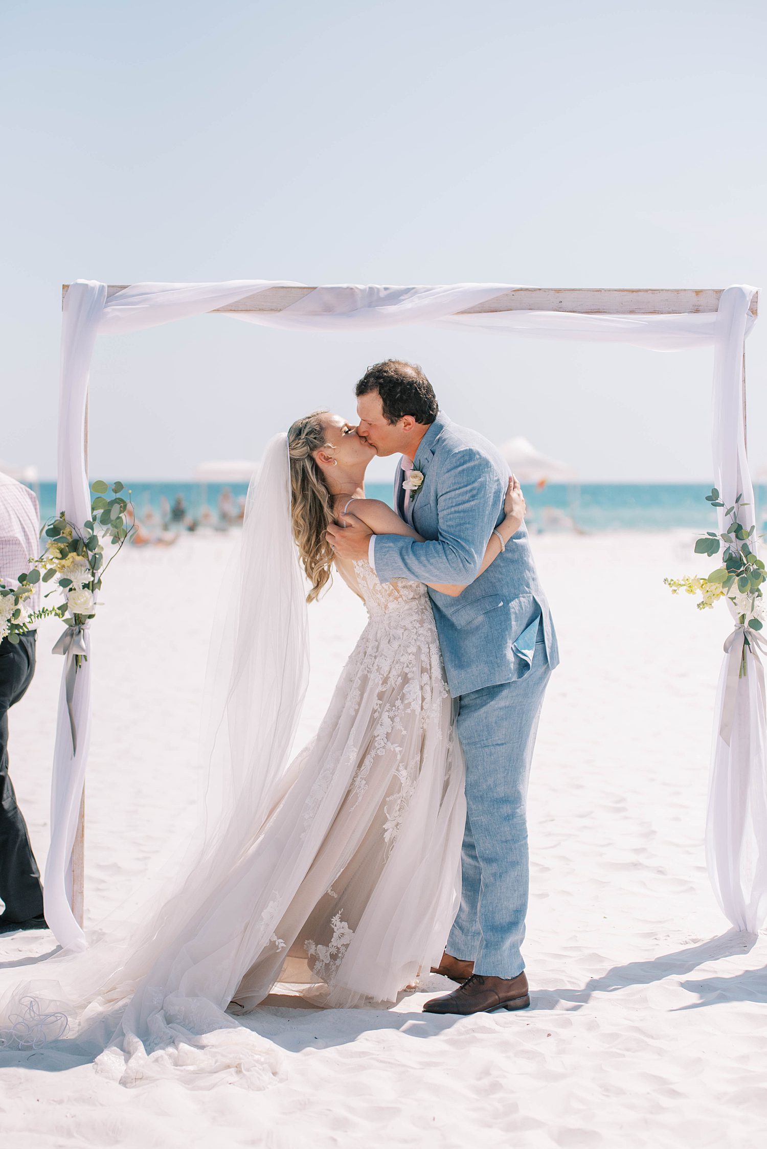 bride and groom kiss during wedding ceremony on the beach 