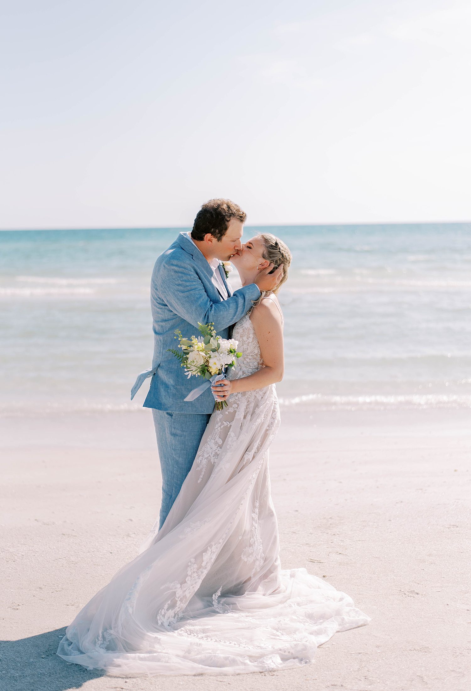 newlyweds kiss on Florida beach while wind moves bride's gown