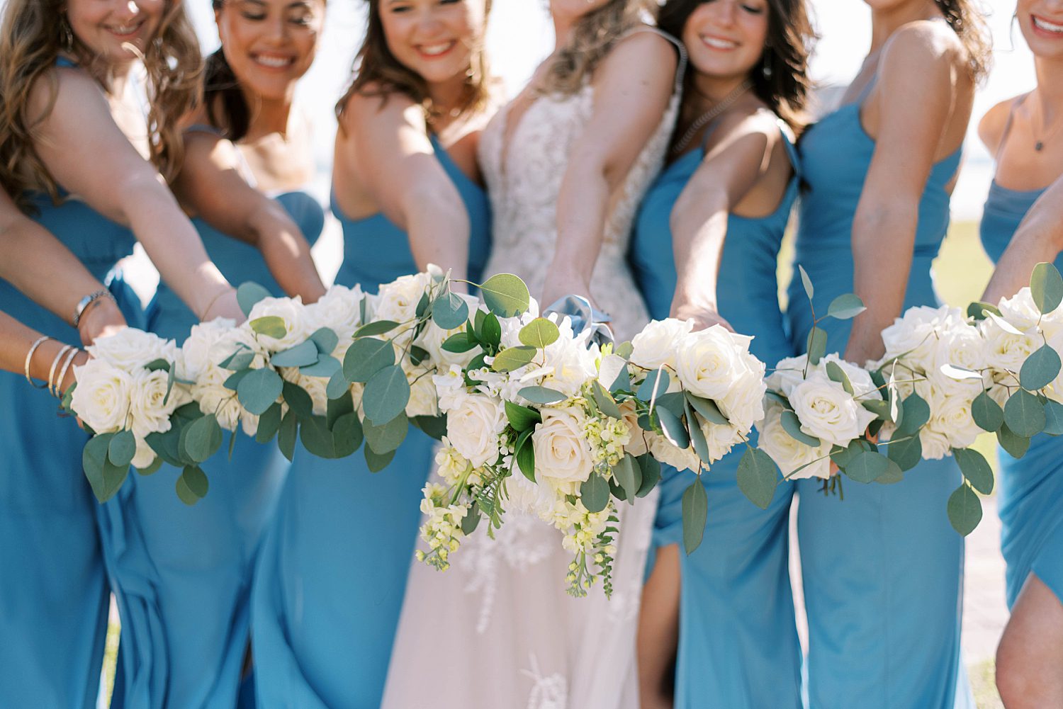 bride and bridesmaids in blue gowns hold white bouquets