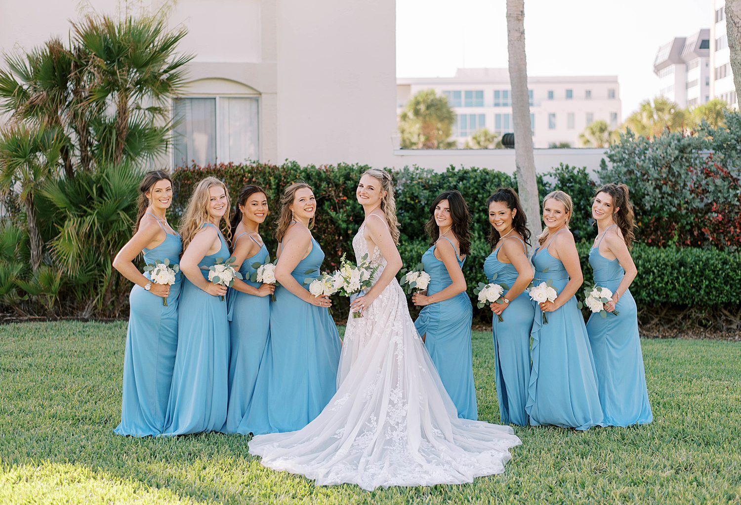 bride poses with bridesmaids in blue gowns looking over shoulder 