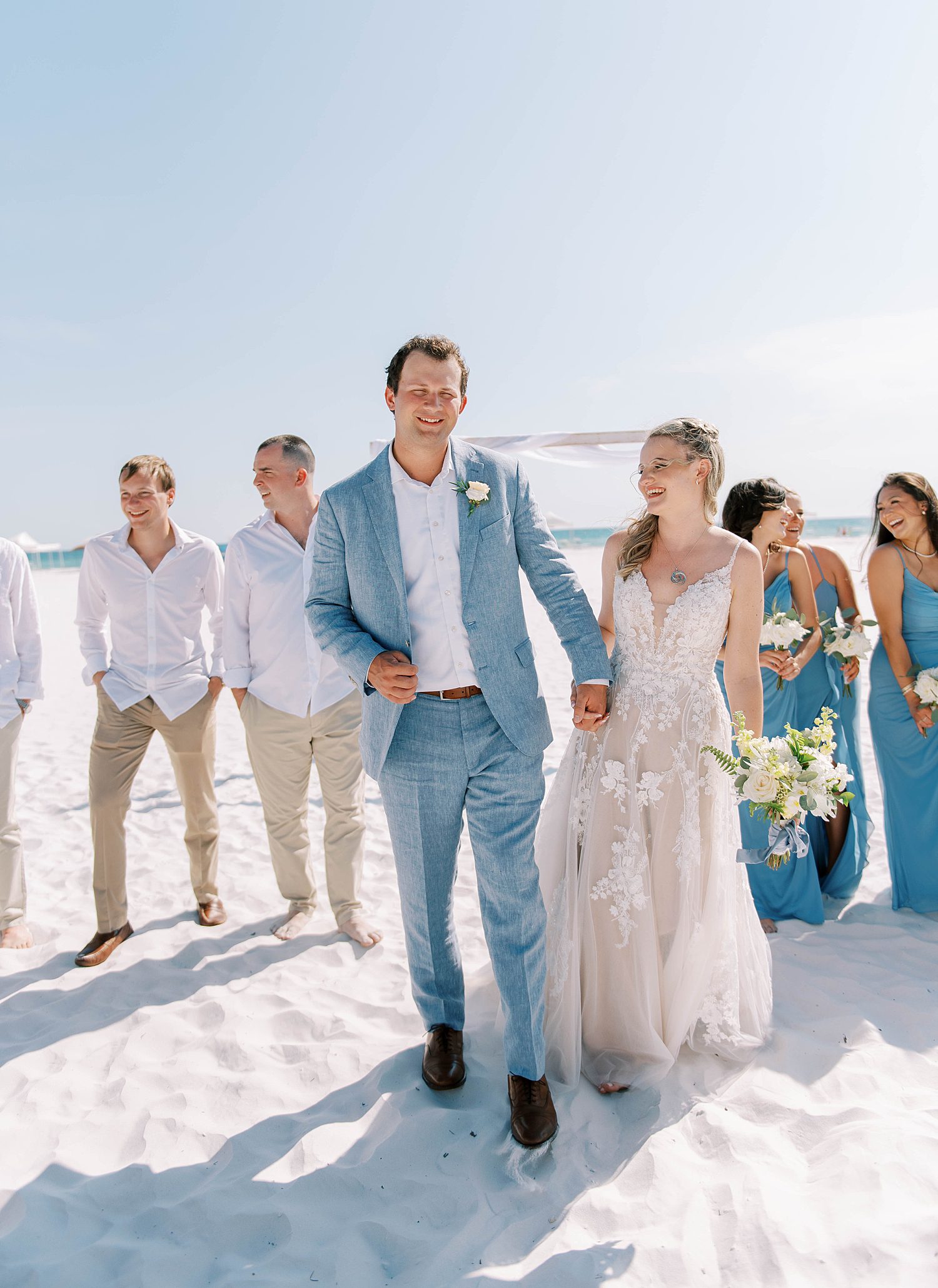 newlyweds walk on beach with bridal party during beach wedding photos