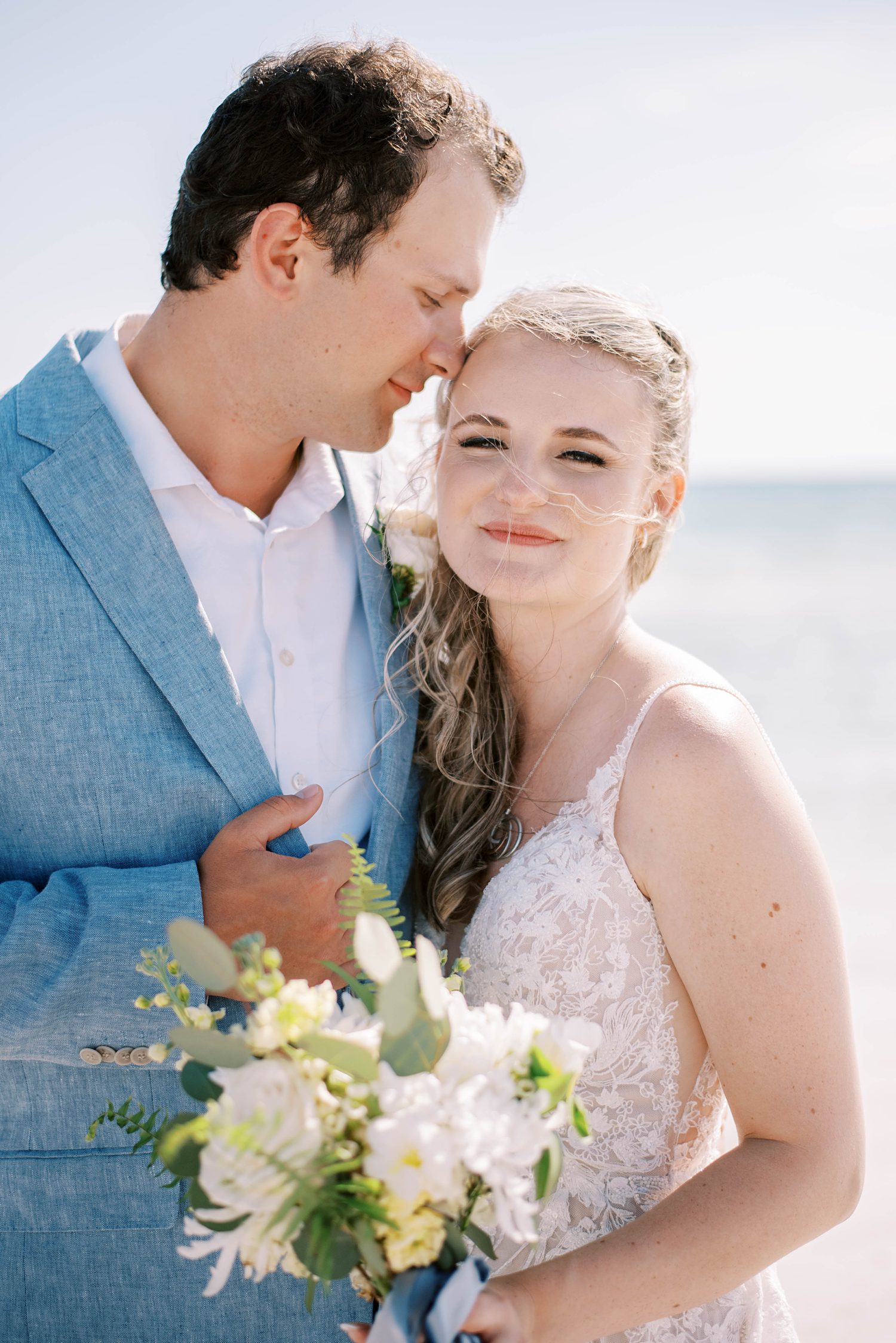 groom nuzzles bride's forehead during beach wedding photos